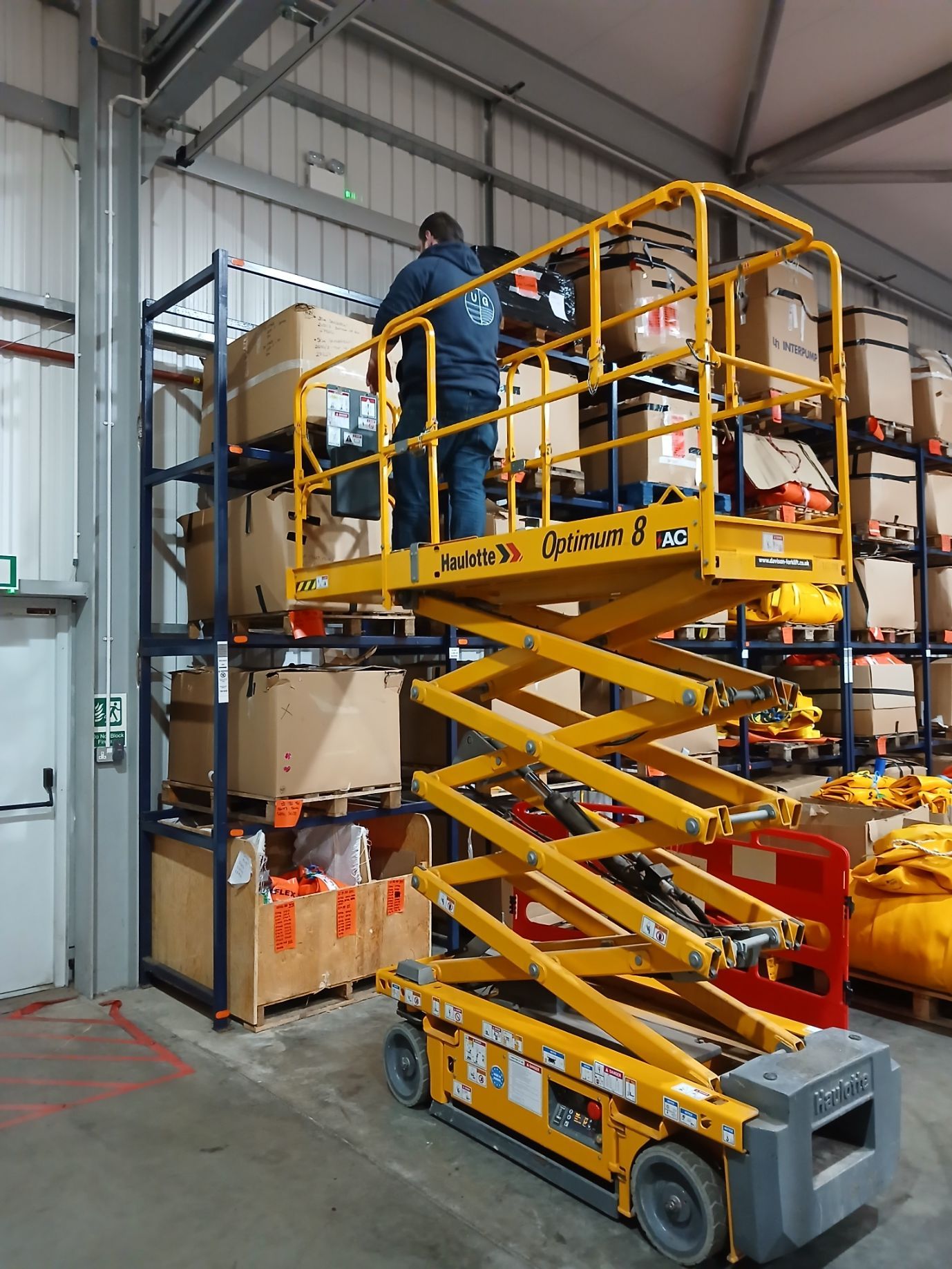 Man on yellow scissor lift reaching for items on warehouse shelving.