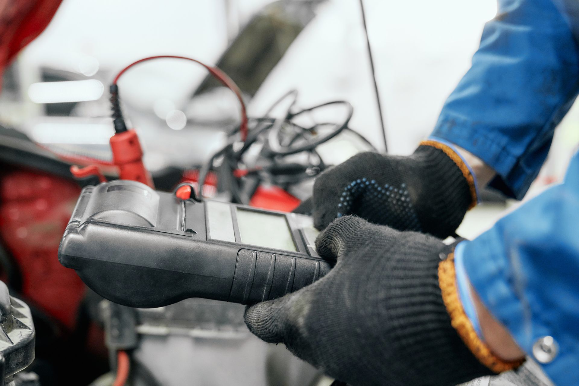 A person is holding a multimeter in their hands in front of a car.