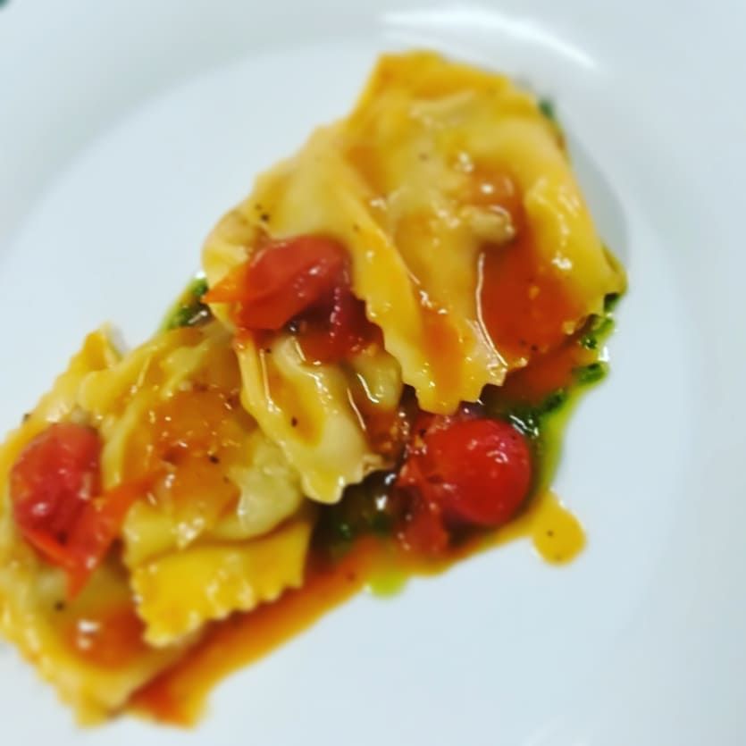 Un piatto bianco condito con ravioli e pomodori