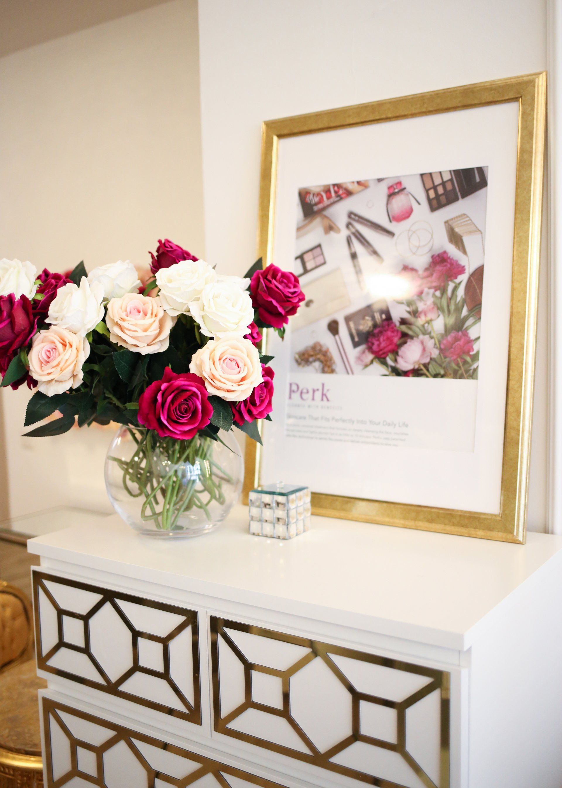 Auf einer weißen Kommode steht eine Vase mit Blumen neben einem gerahmten Bild.