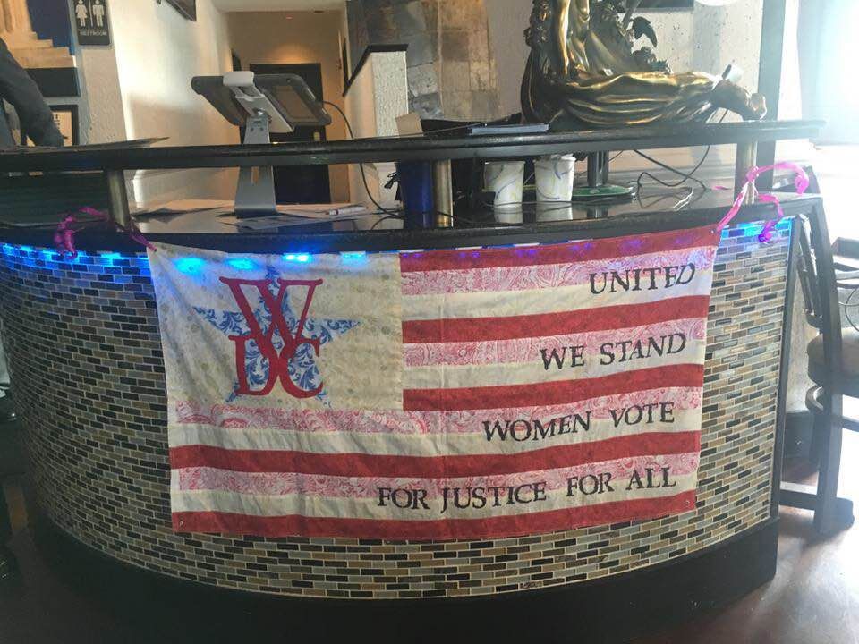A WDC hand quilted flag on a counter that says `` united we stand women vote for justice for all ''