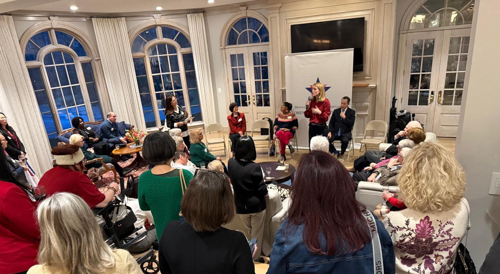 A group of people at WDC event in a large room with arched windows. 
