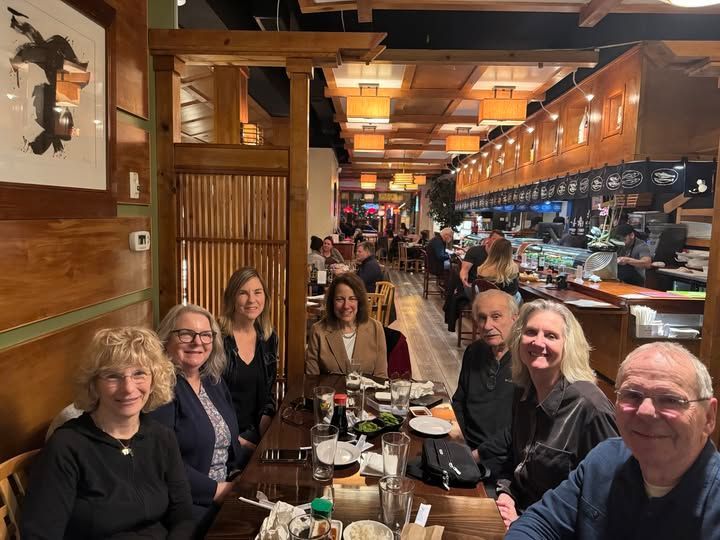 Group of eight people smiling around a wooden table in a dimly lit Japanese restaurant.