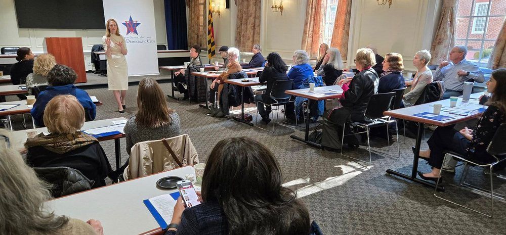 Brooke Lierman giving presentation to a group seated at tables. Inside a meeting room.