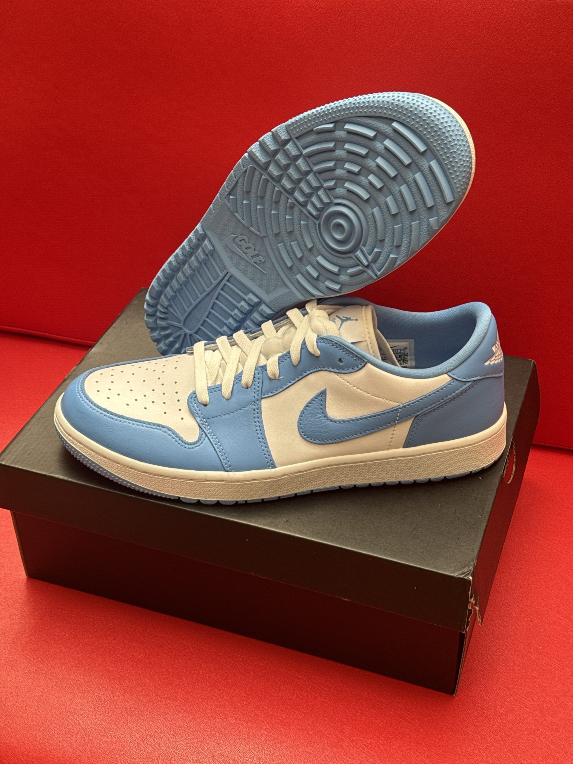 Light blue and white Air Jordan 1 Low sneaker sits on a black box, sole visible above.