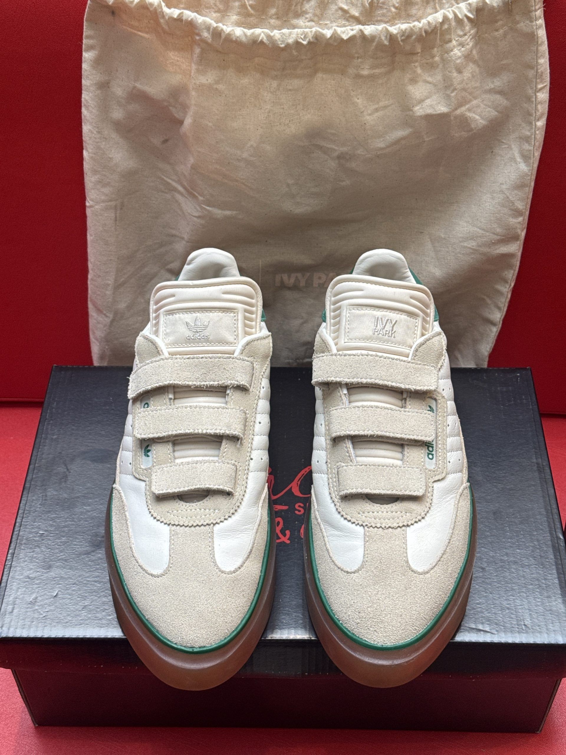 Beige Adidas sneaker with velcro straps, on a black box, with a red background.