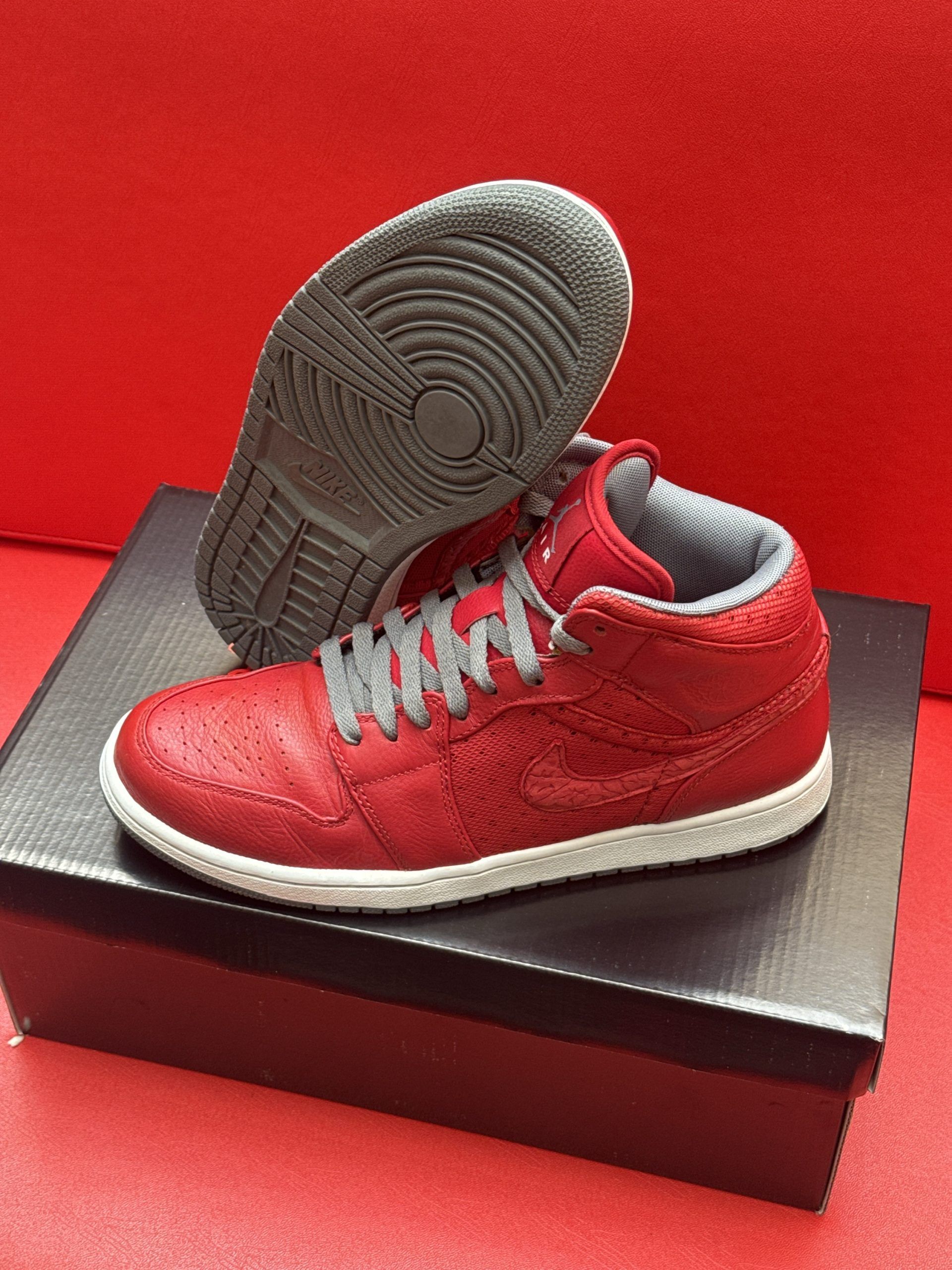 Red and white Air Jordan sneakers on a shoebox, with one sole facing upward against a red backdrop.