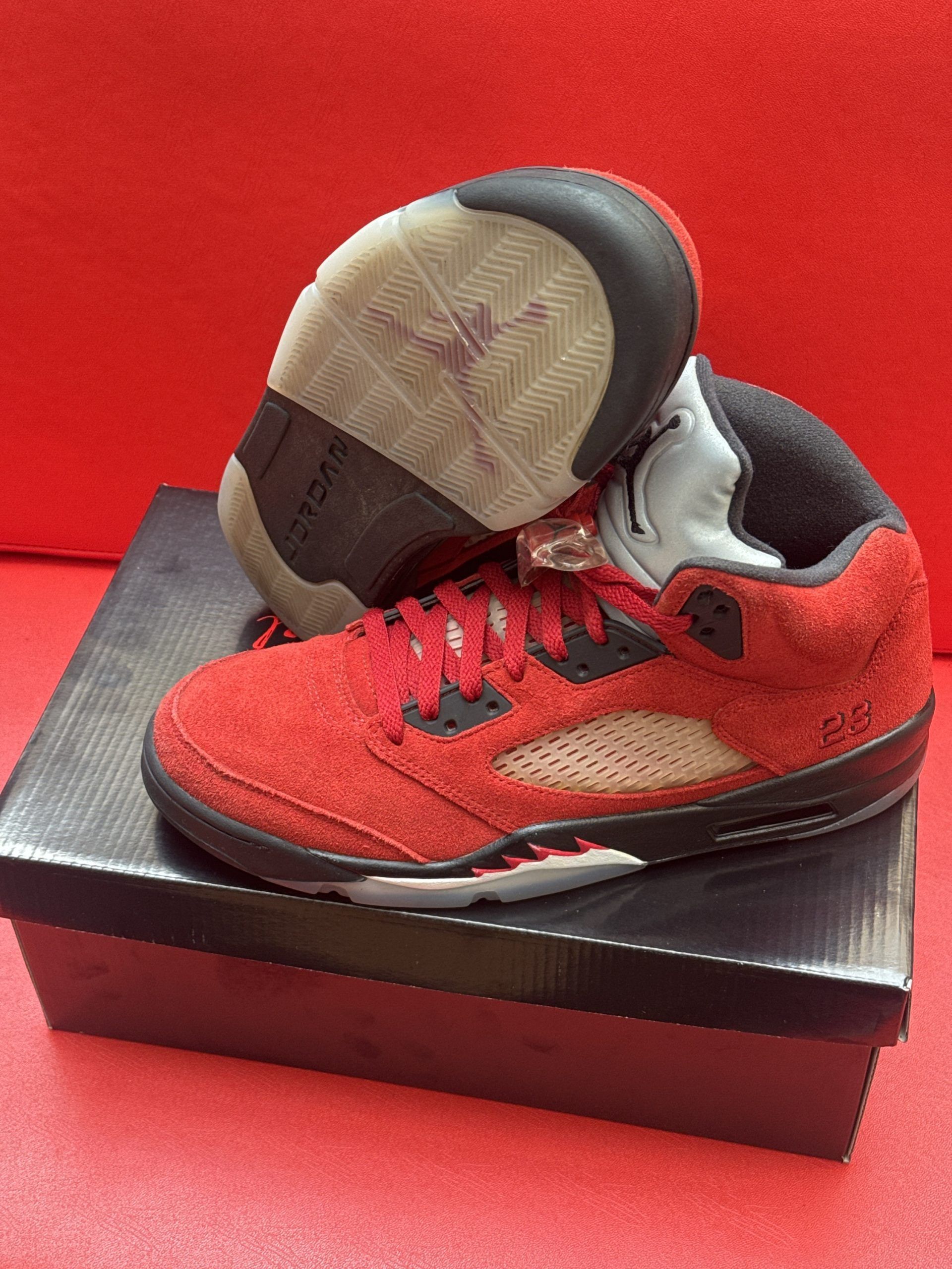 Red and black Air Jordan 5 sneakers, partially on a shoebox.