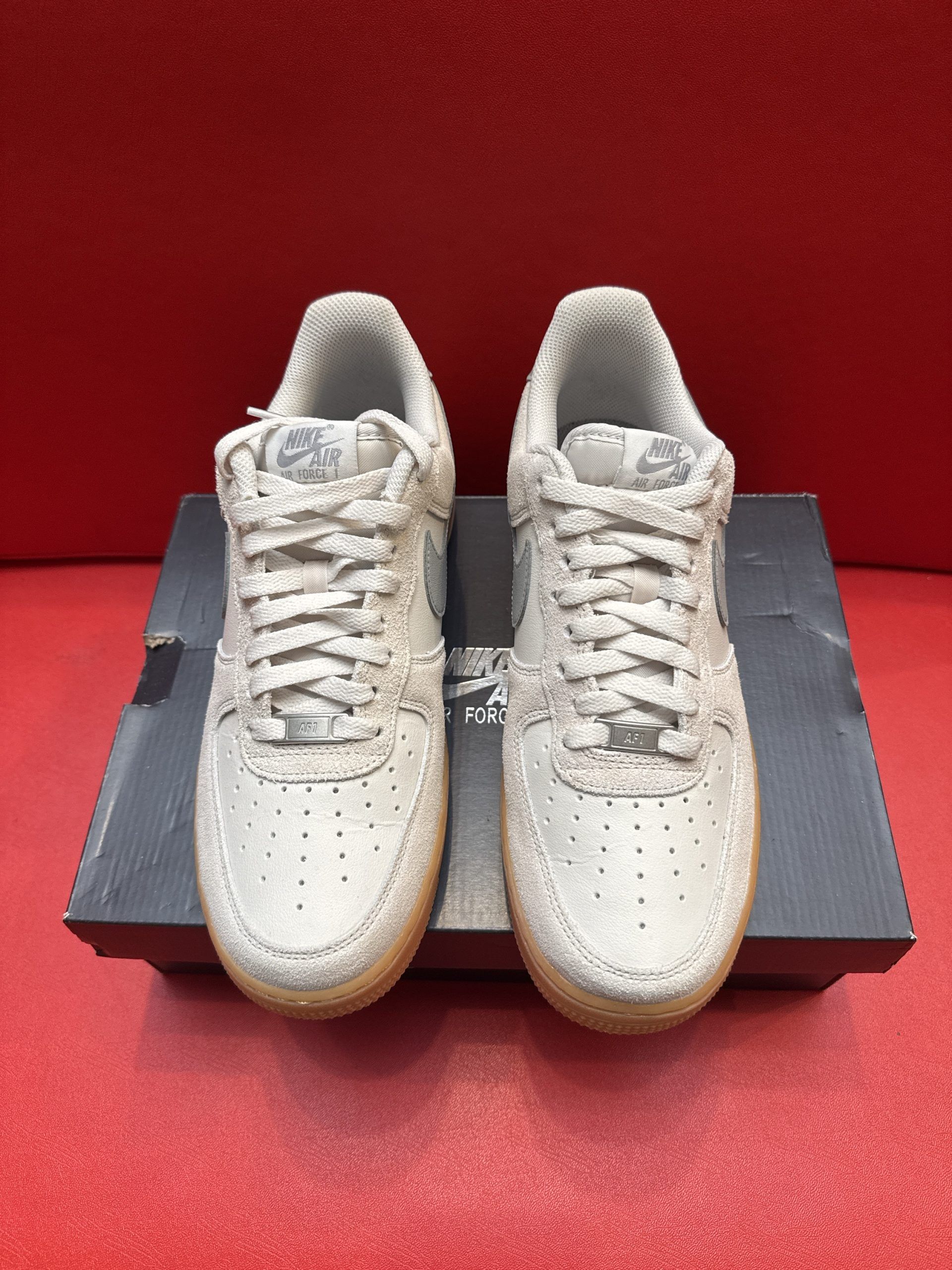 Gray Nike Air Force 1 sneakers with brown sole on a black box. The other shoe's sole is visible.