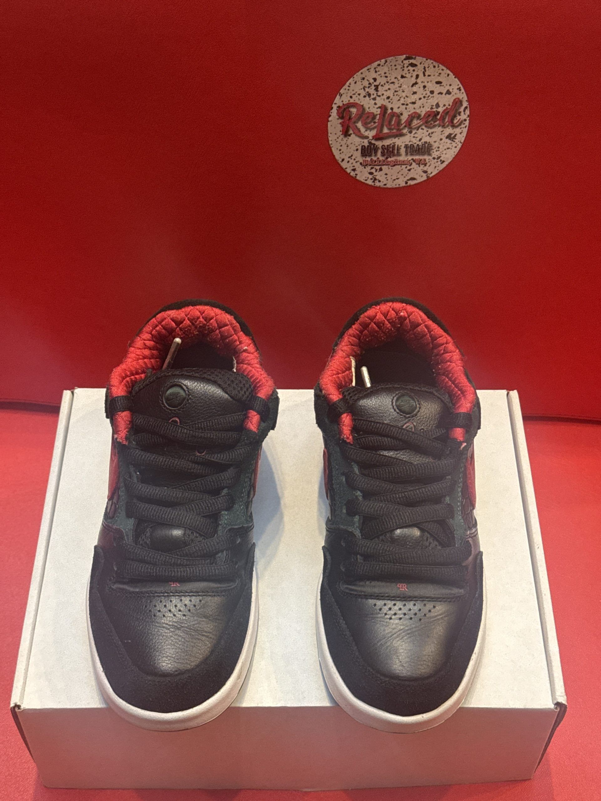 Black Nike sneakers with red accents, on a white box against a red backdrop.