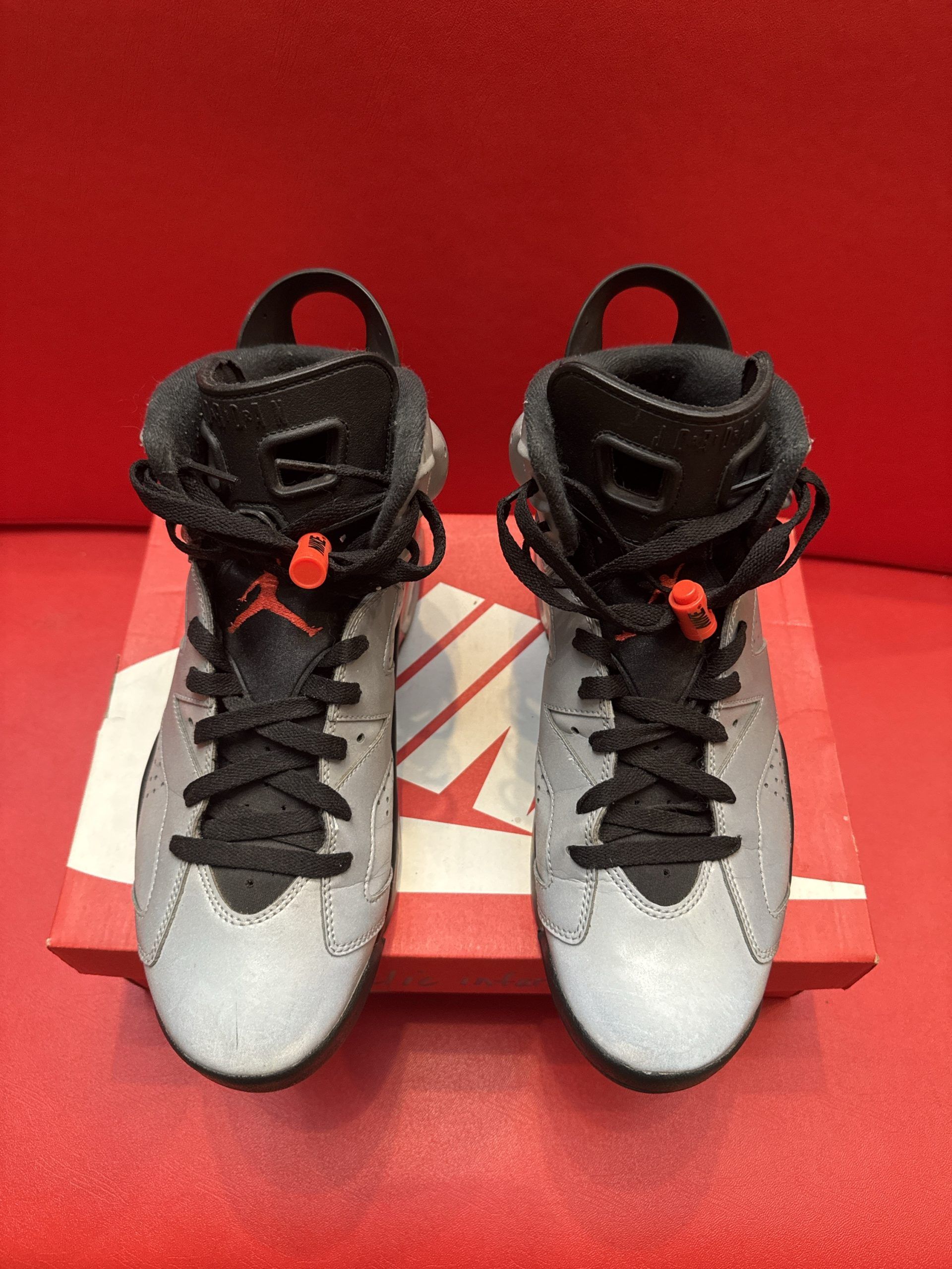 Gray, orange, and black Air Jordan 6 sneakers on a red Nike box; one shoe's sole visible.