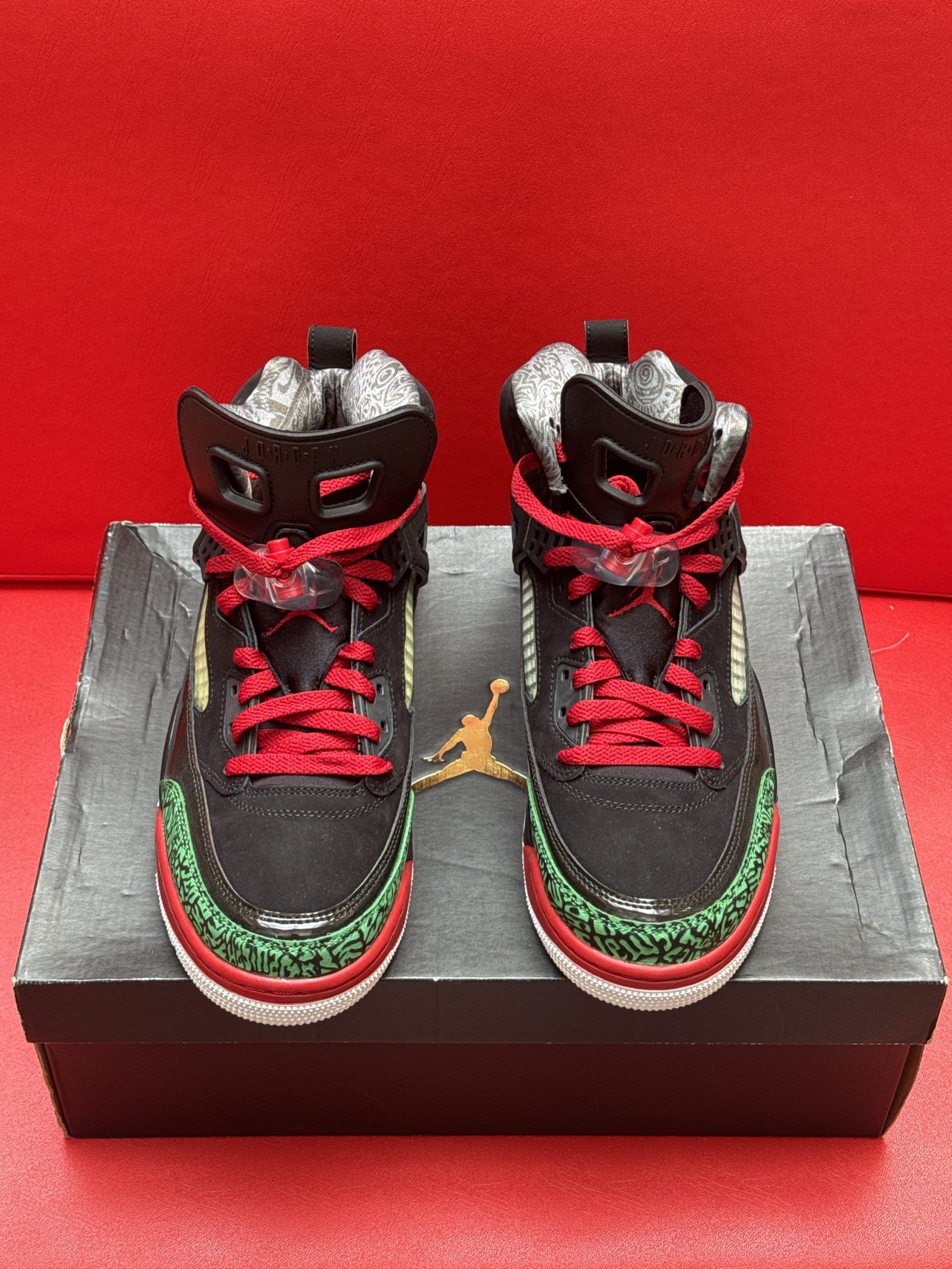 Black, red, and green Air Jordan sneakers on a box; one shoe displayed sole-up with green and white details.