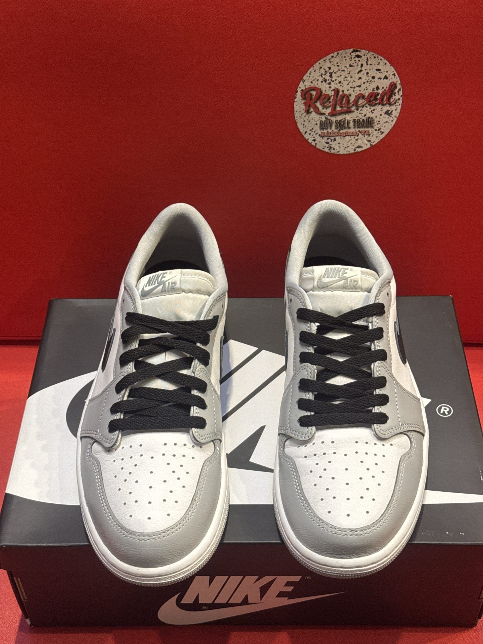Air Jordan 1 Low sneakers, gray and white with a black Nike swoosh, on a black Nike shoe box.