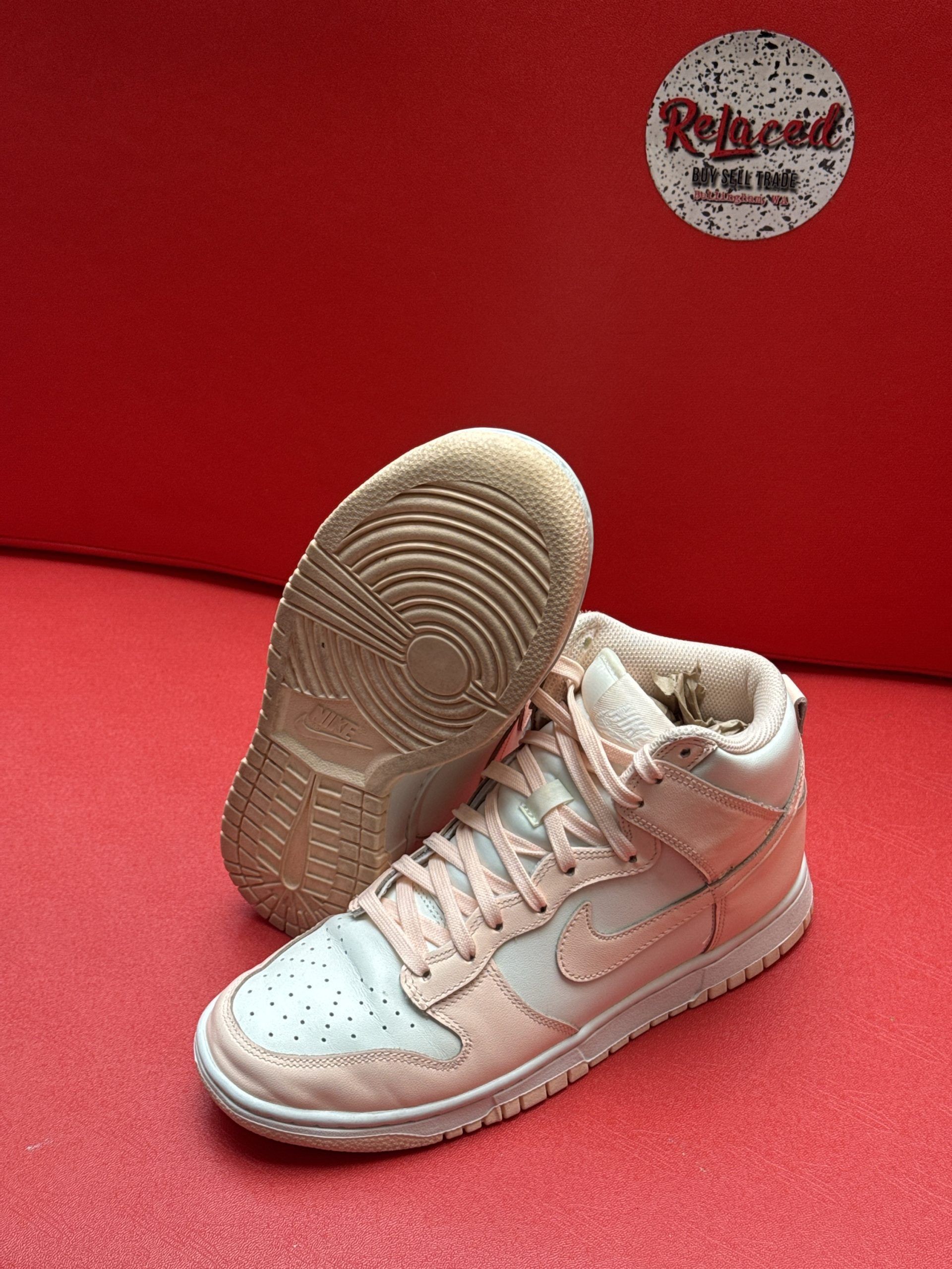 Pair of light pink Nike high-top sneakers with a white sole, set on a red surface.