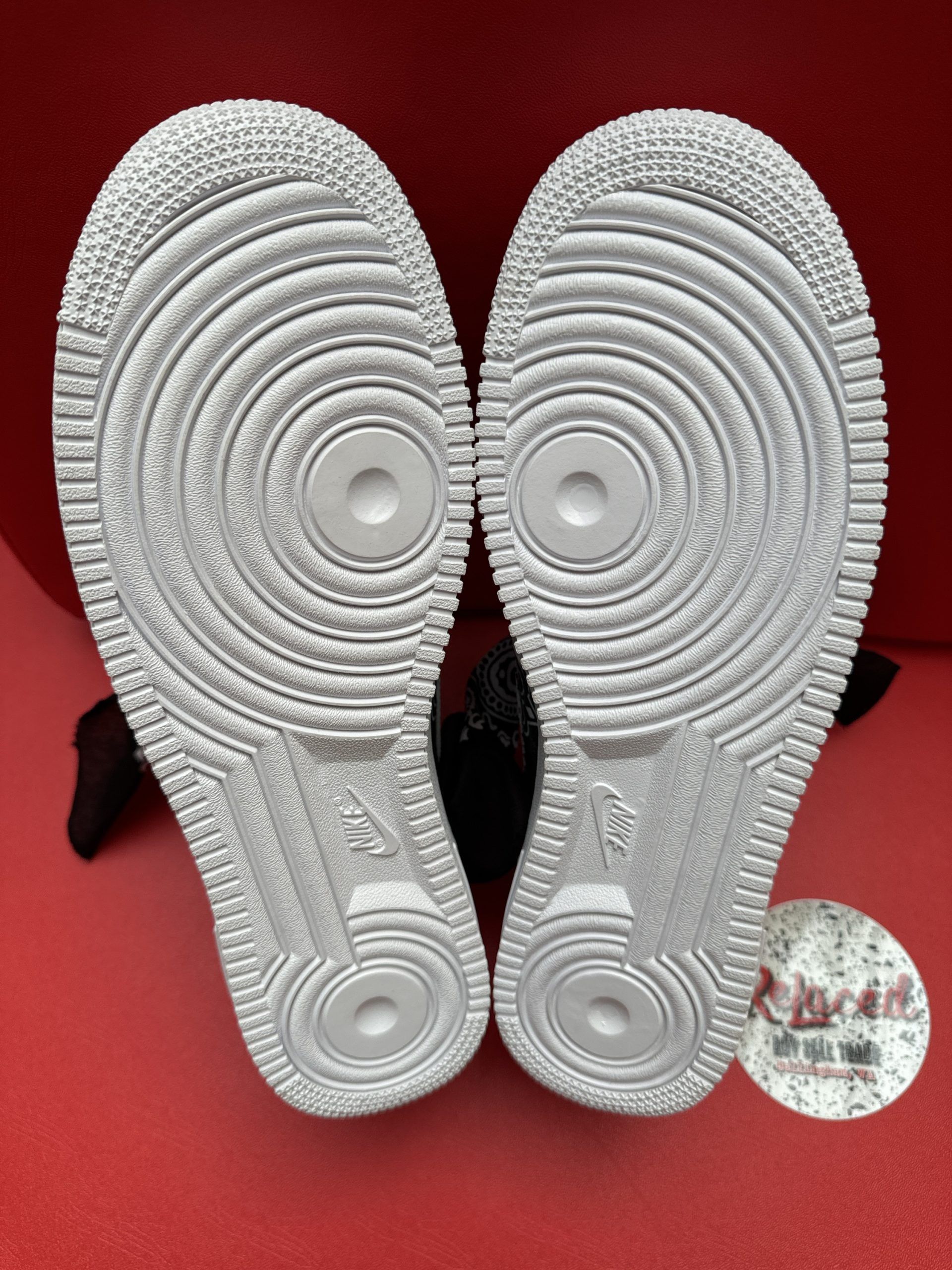 White Nike Air Force 1 sneakers customized with black bandana accents, sitting on a white pedestal with a matching bandana.