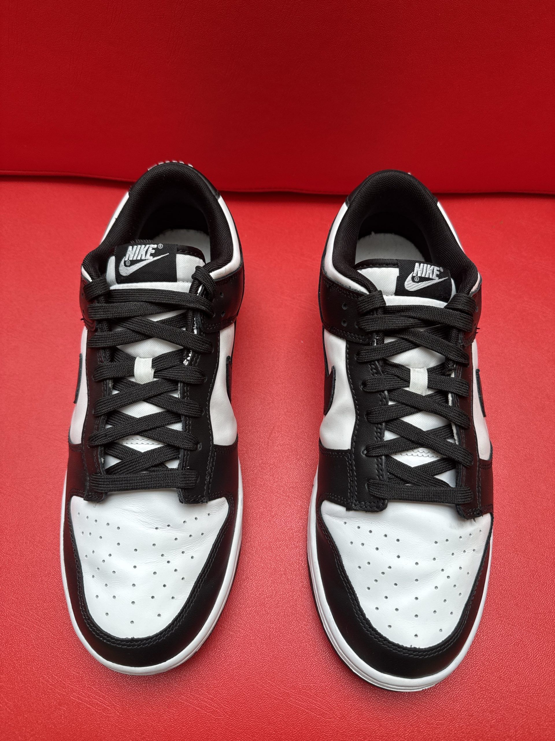 Black and white Nike Dunk Low sneakers, one upright, one showing the sole, on a red surface.