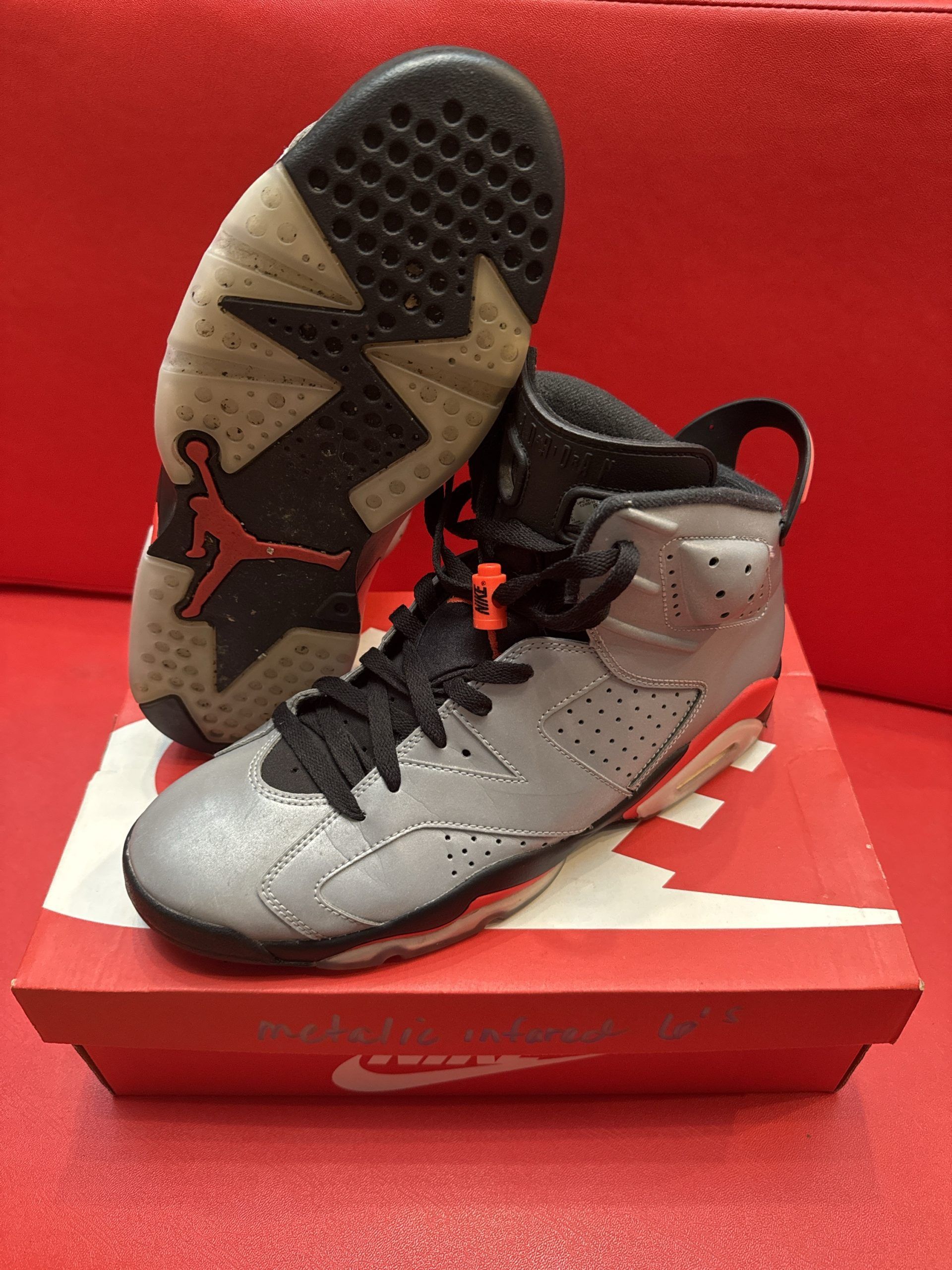 Gray, orange, and black Air Jordan 6 sneakers on a red Nike box; one shoe's sole visible.