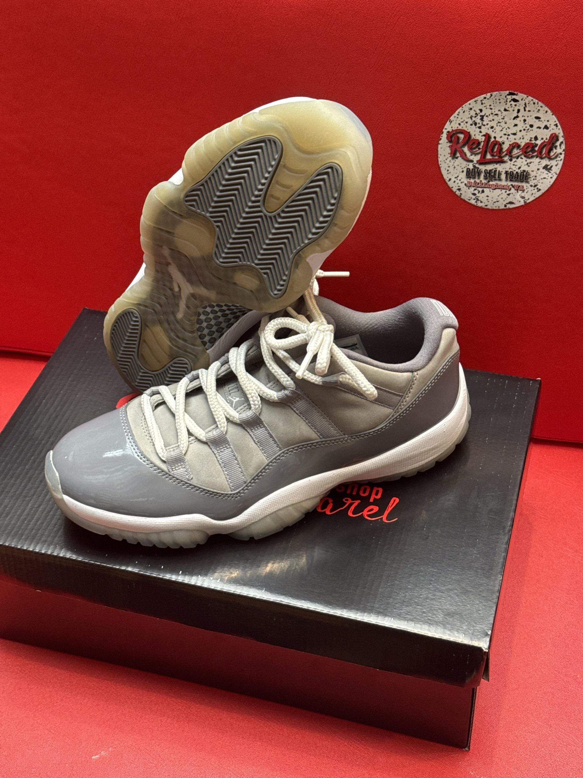 Gray Air Jordan 11 Retro low-top sneakers on a black box, with a red background.