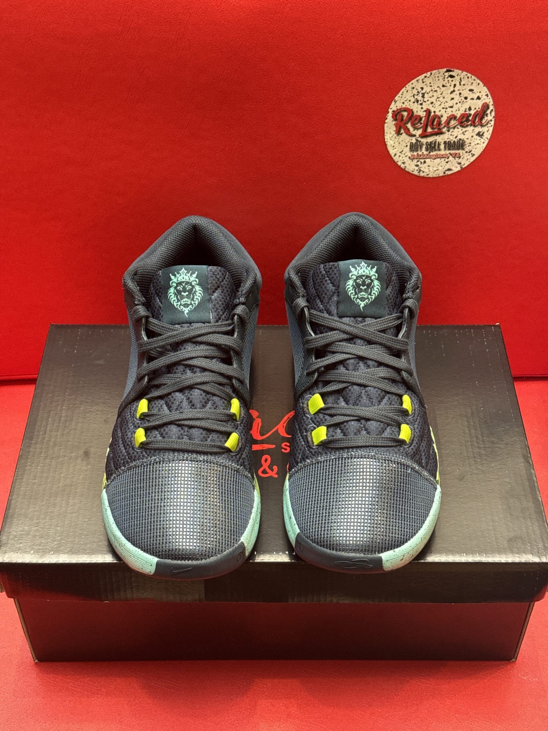 A pair of blue and green Nike basketball shoes on top of a black shoebox, against a red background.