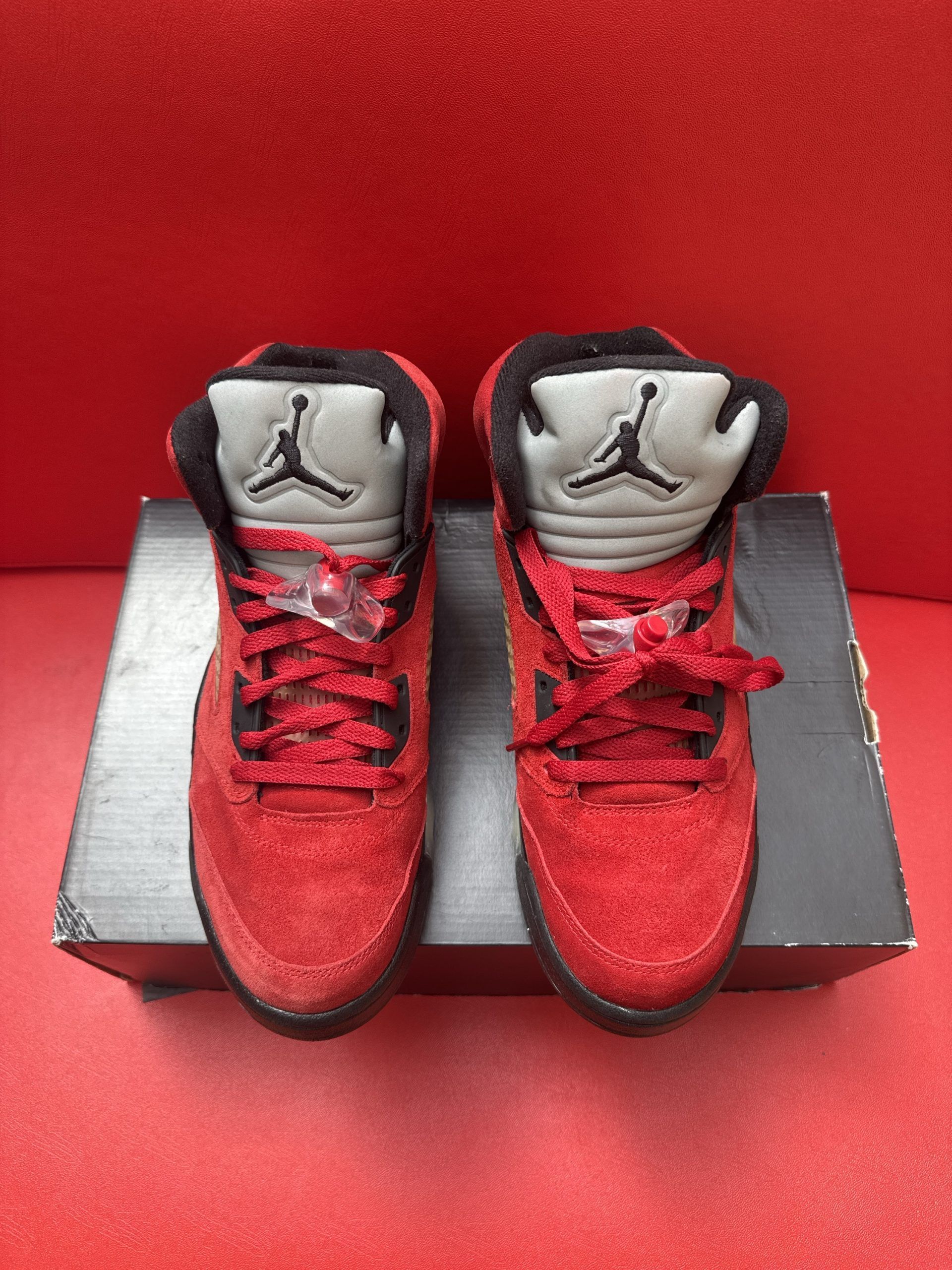 Red Air Jordan 5 sneakers, partially on a black shoebox, with a visible Jumpman logo on the sole.