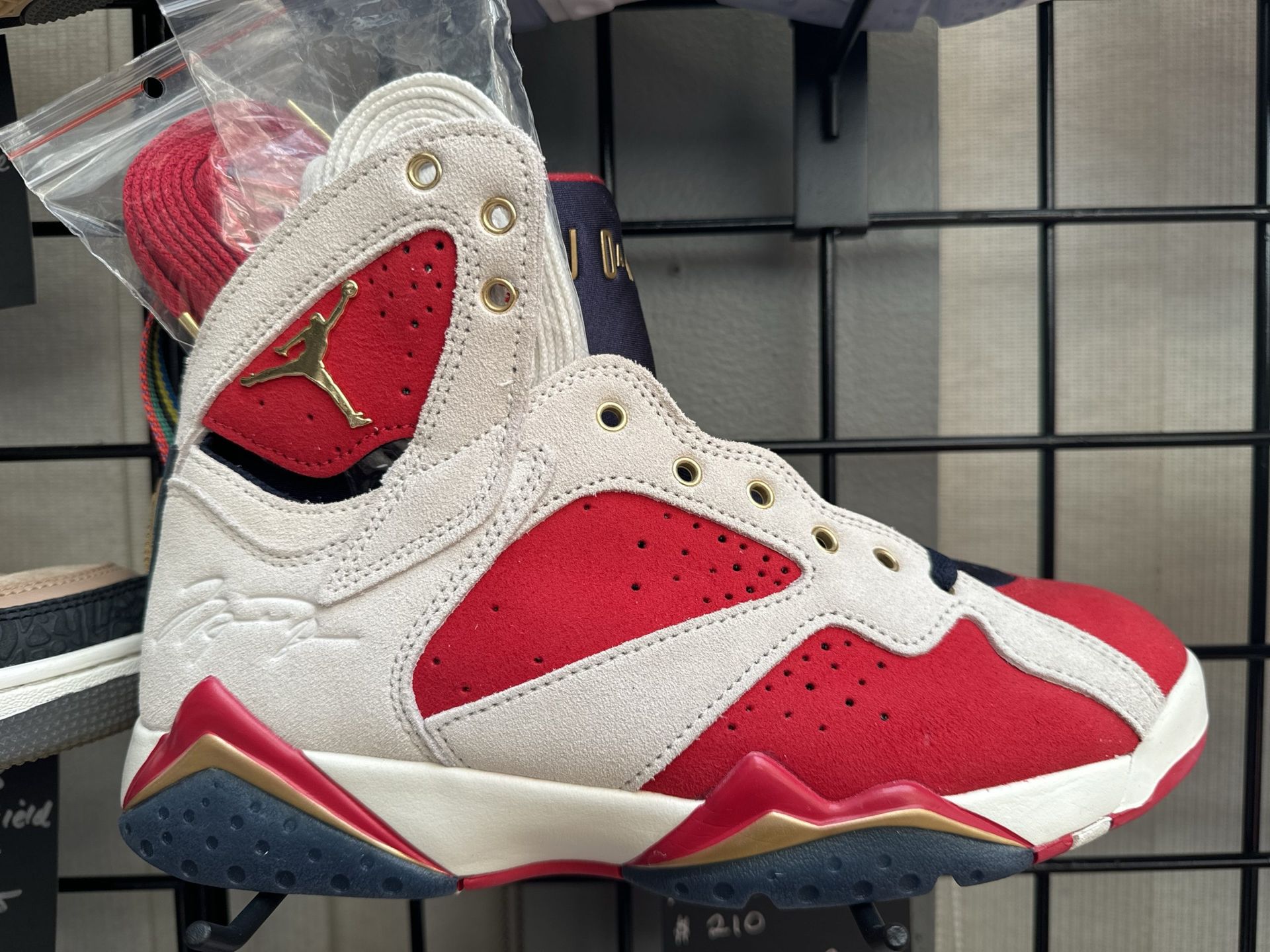 Pair of red, blue, and tan Air Jordan 7 sneakers on top of a shoe box with a red background.