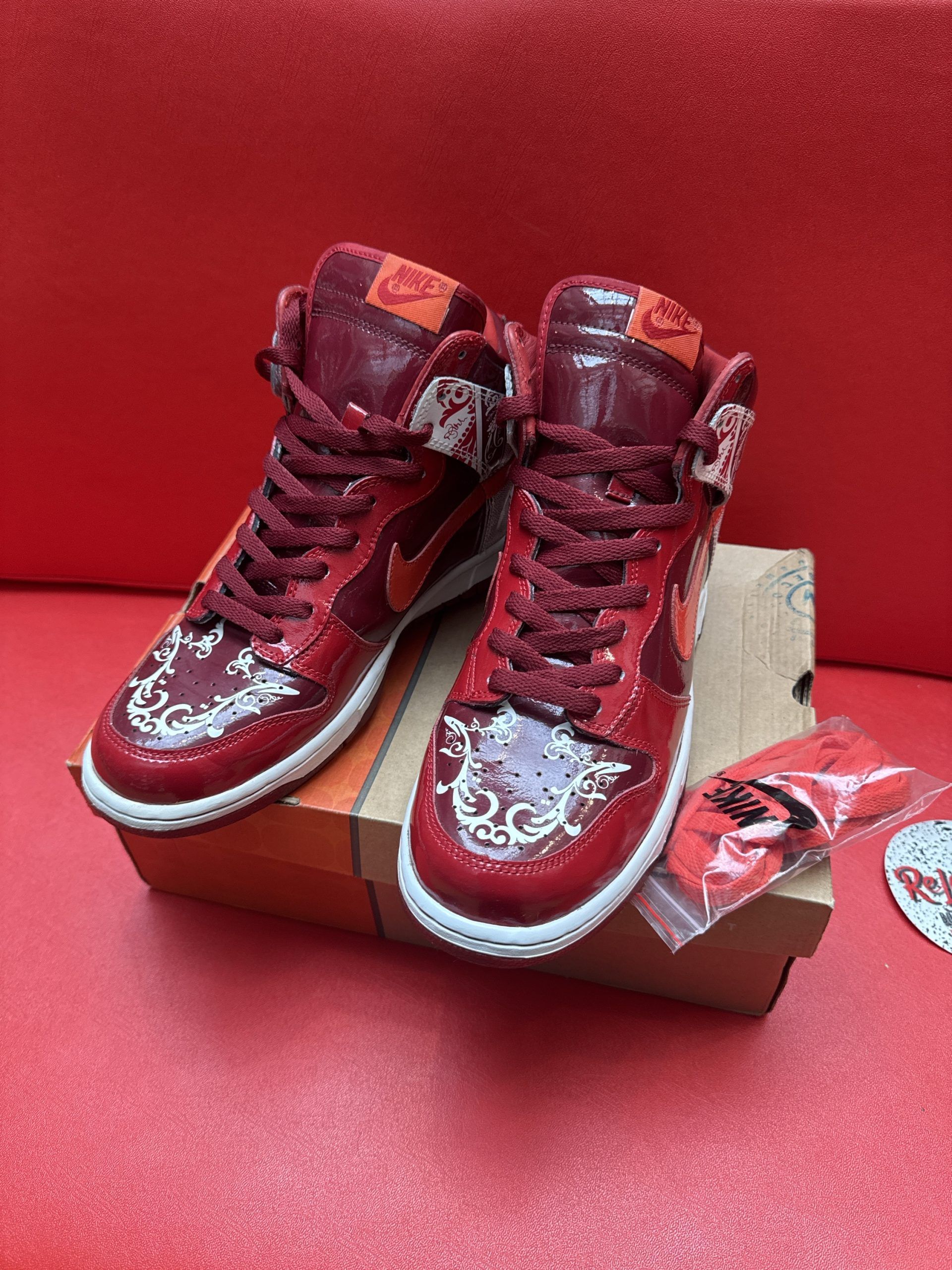 Red Nike Dunks, box, and extra laces on a red surface.