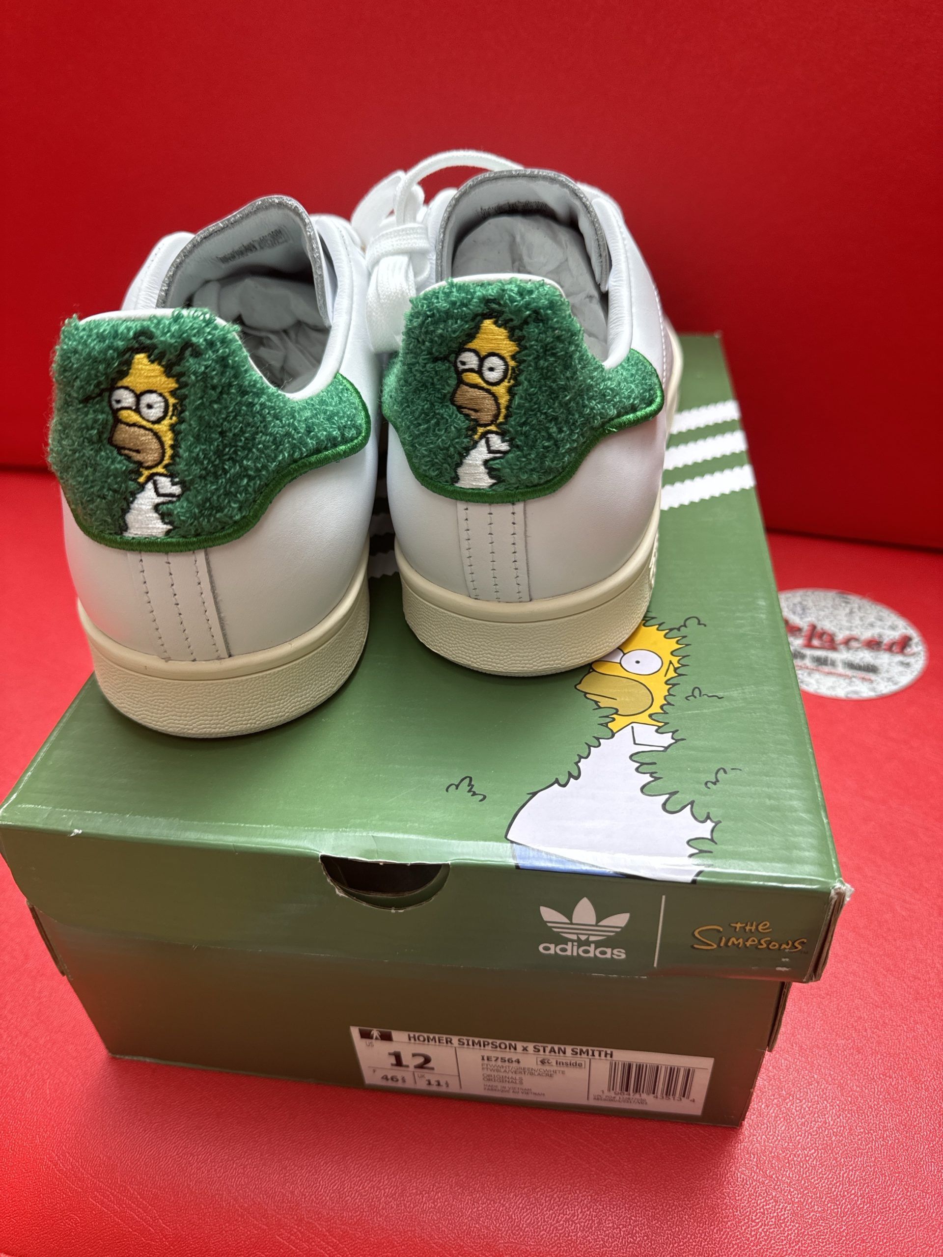 White Adidas Stan Smith sneakers with green accents on a green box and red surface.