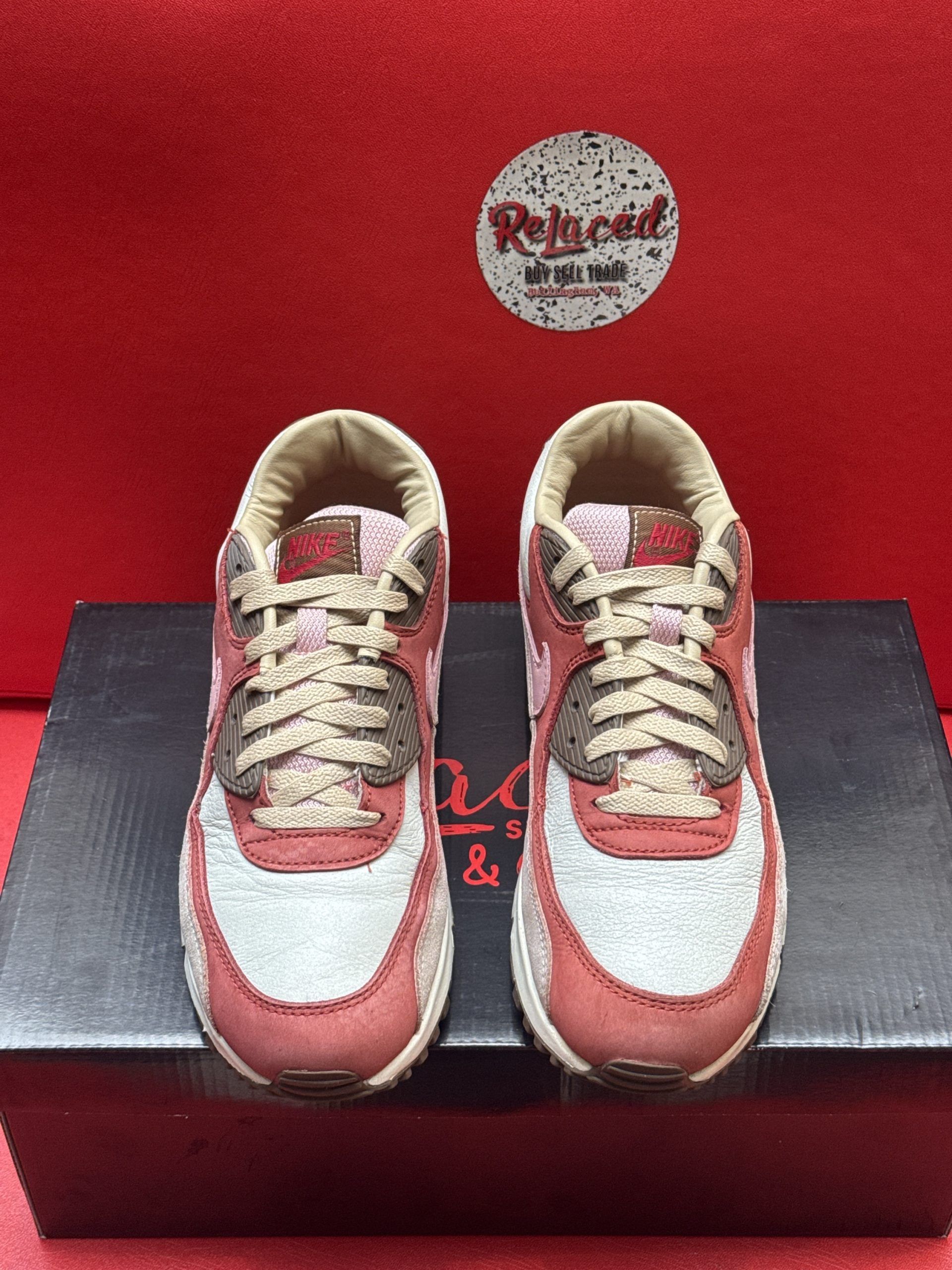 Nike Air Max 90 sneakers, red and tan colors, on a black shoebox with a red background.