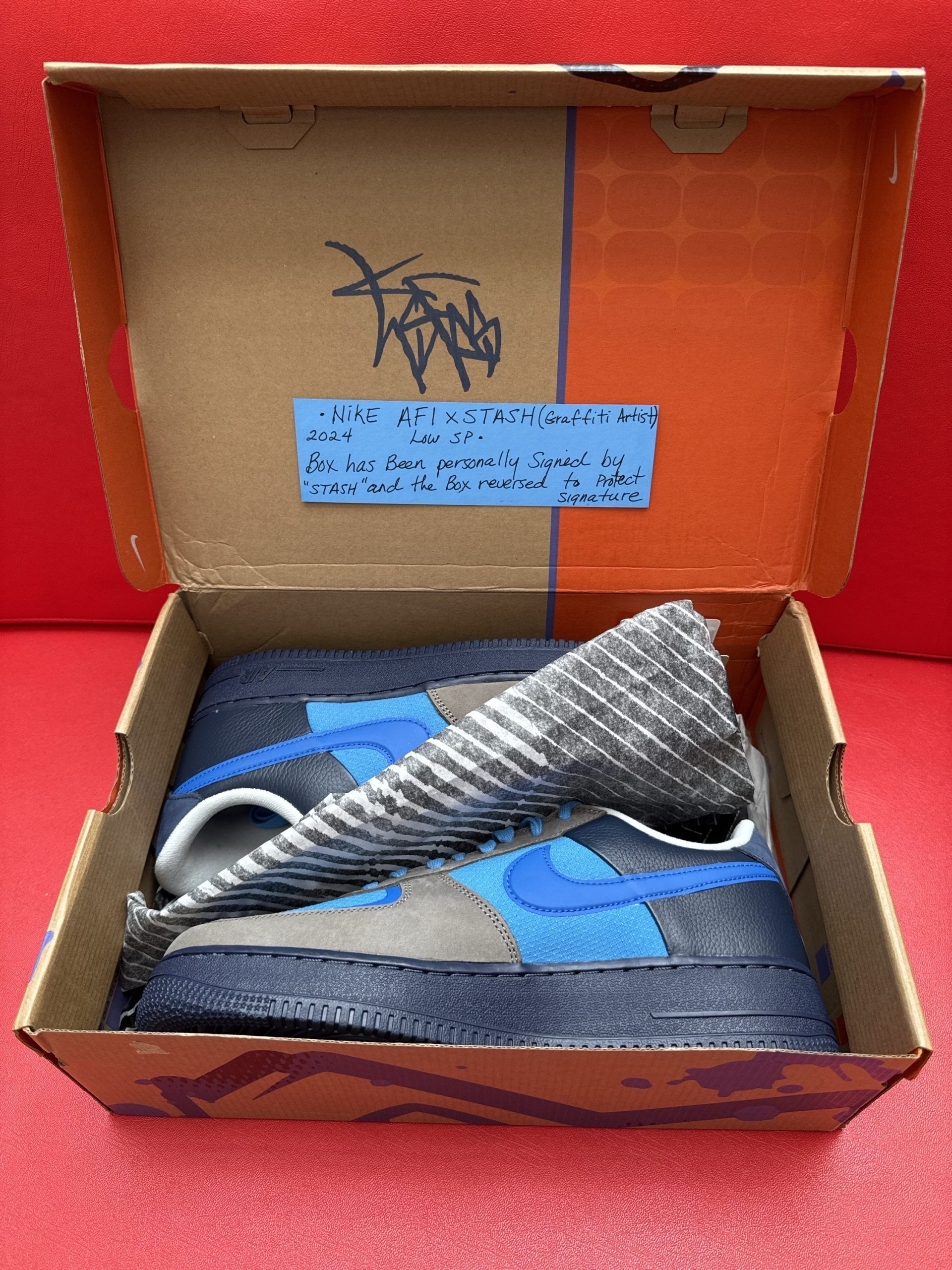 Blue and gray Nike Air Force 1 sneakers on splatter-painted box, against a red background.