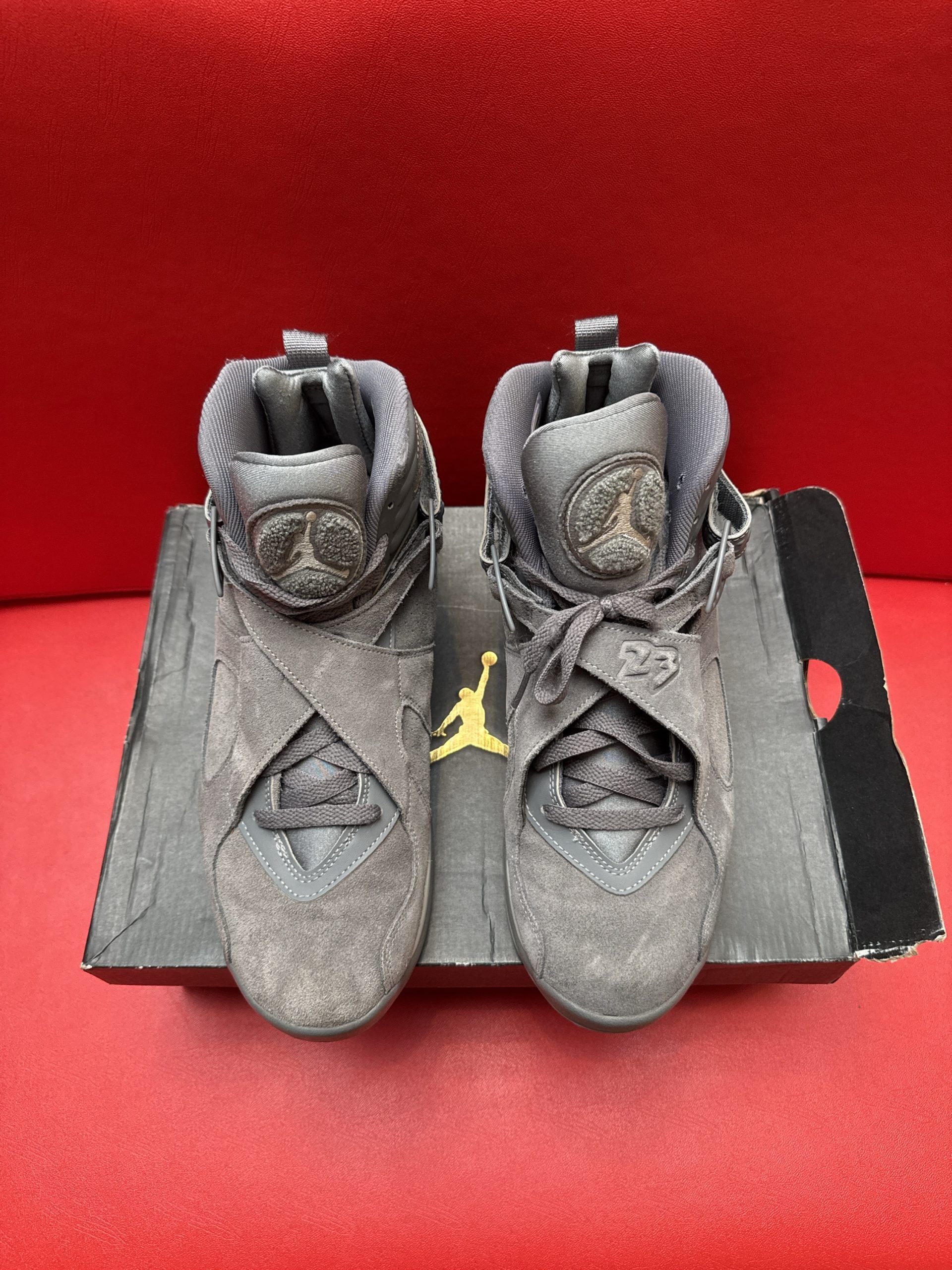Gray Air Jordan 8 sneakers on a black shoe box against a red background.