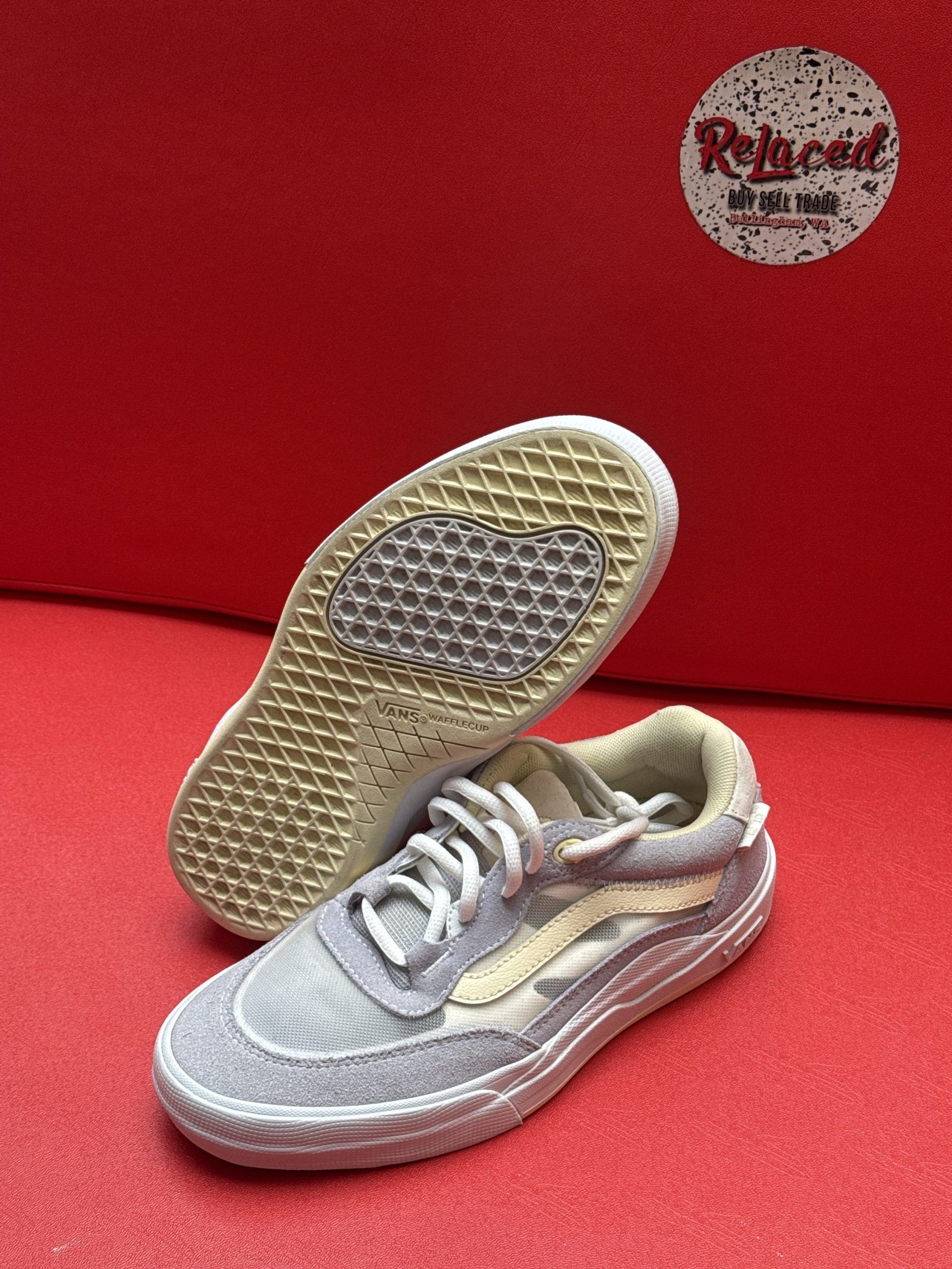 Gray and beige Vans sneaker, sole up. Red backdrop.