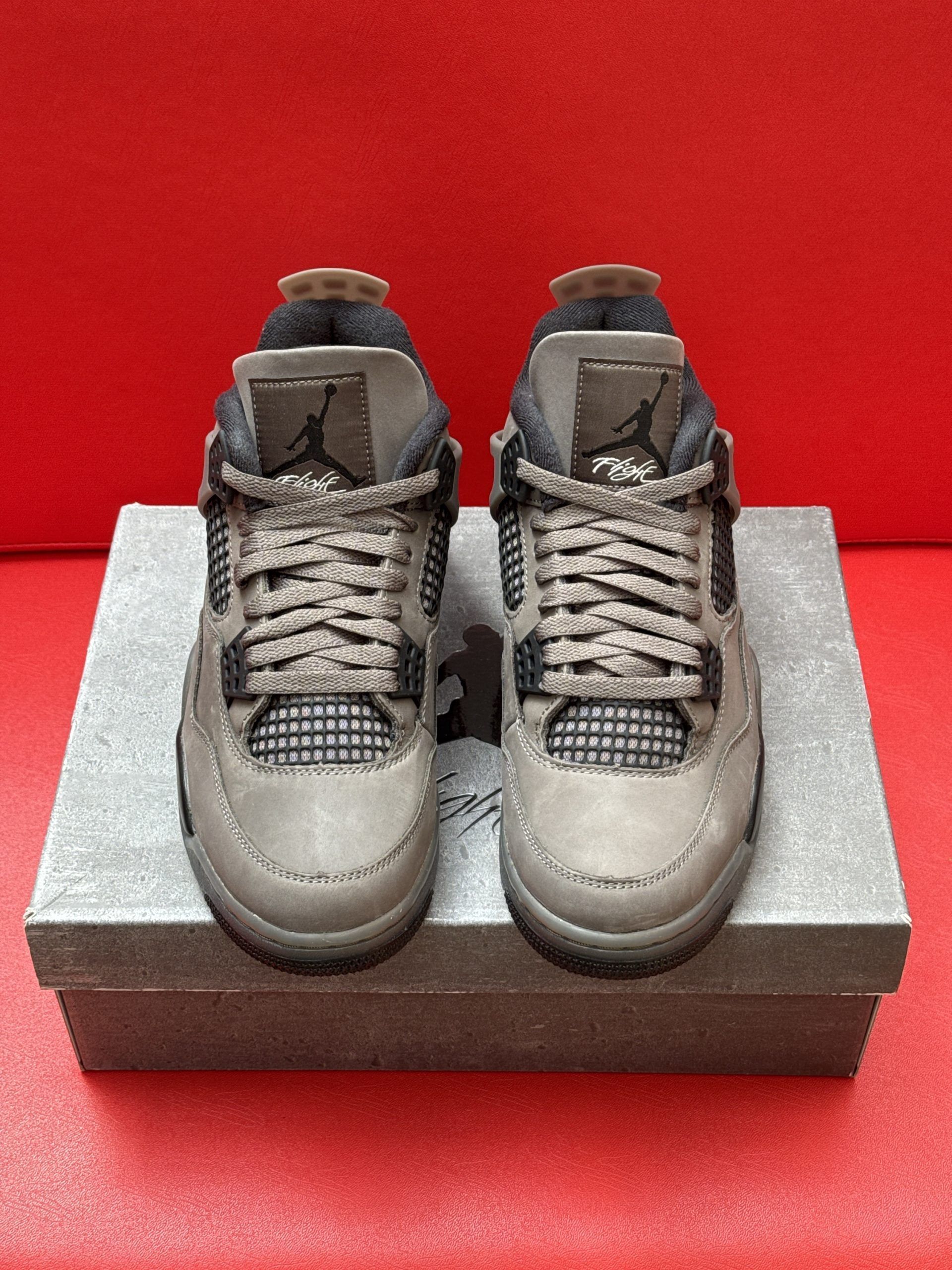 Gray and black Air Jordan 4 sneakers on a gray box, with the sole visible. Red background.