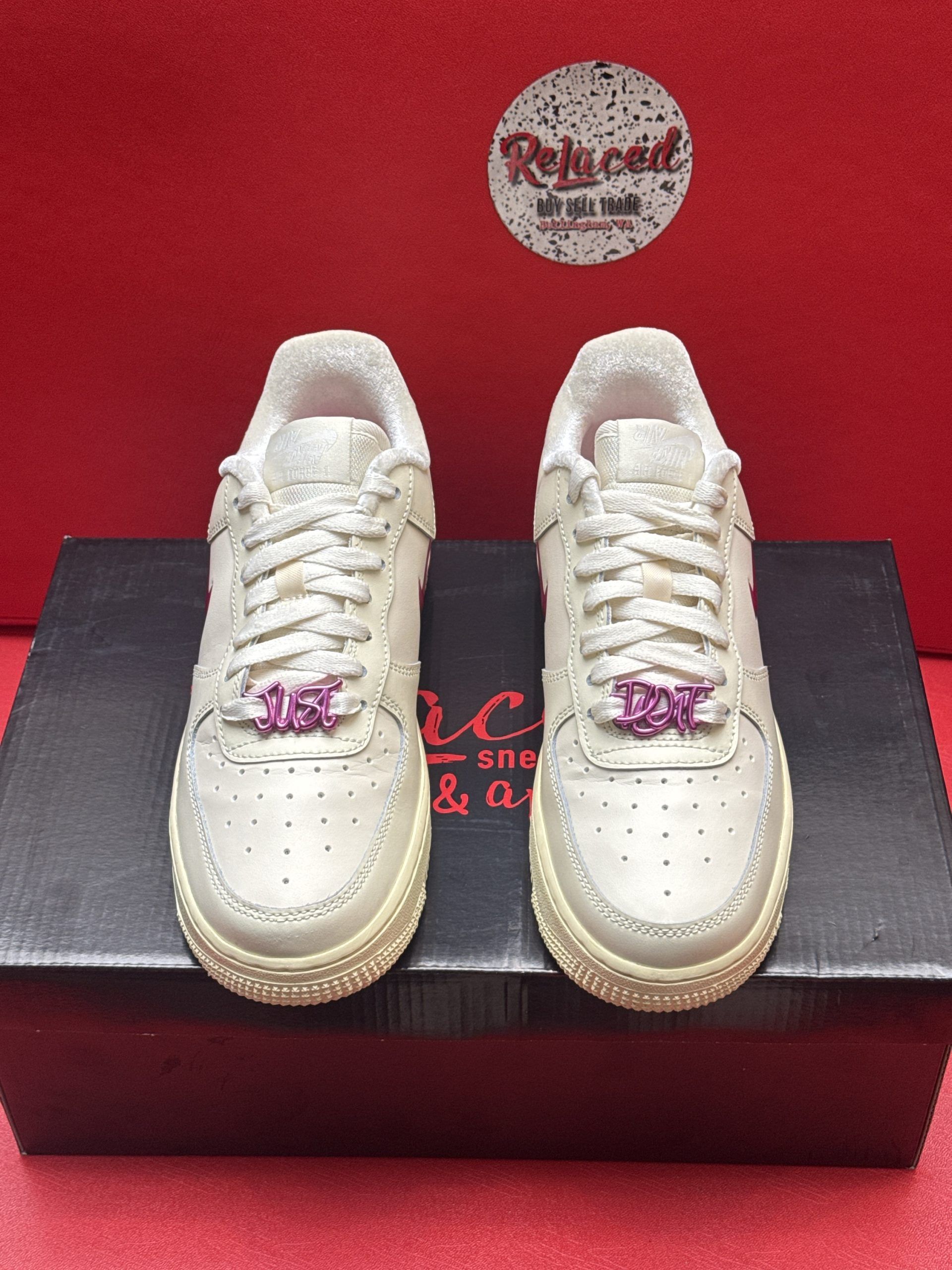 Cream-colored Nike Air Force 1 sneakers with a purple swoosh and laces, set on a dark box against a red backdrop.