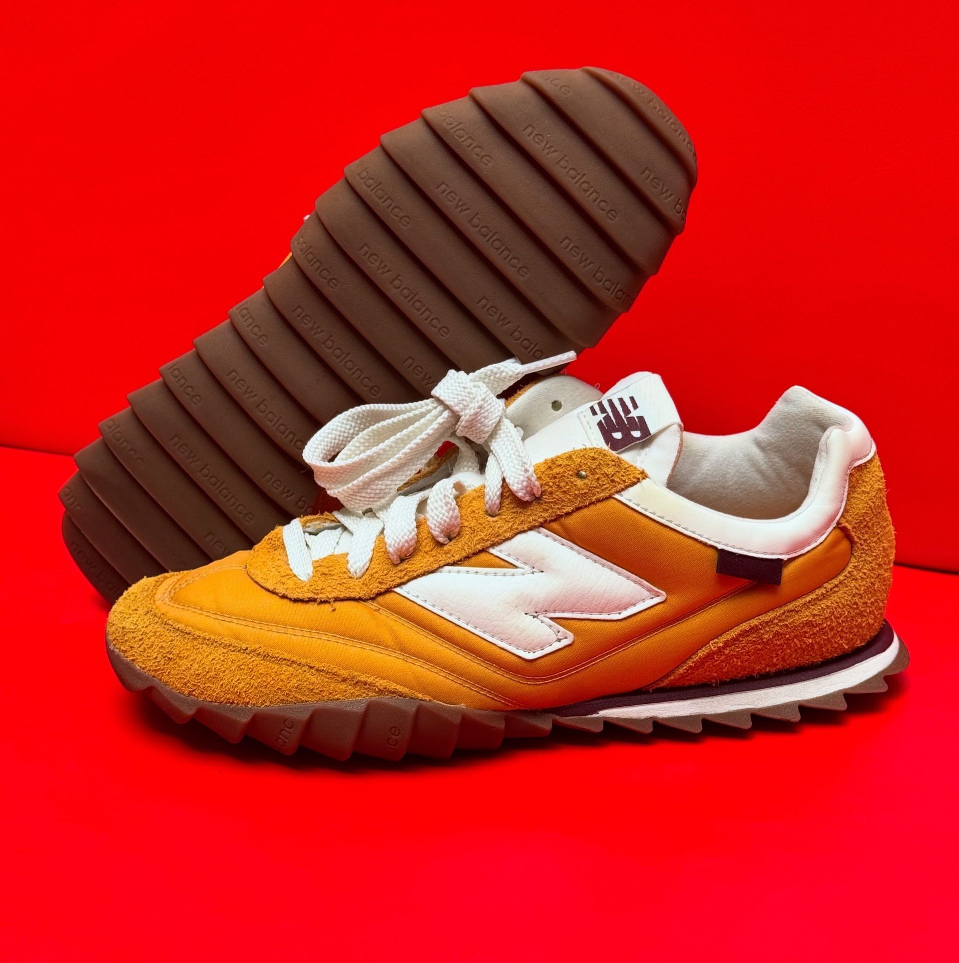 Yellow and white New Balance sneaker with brown sole on a red background.