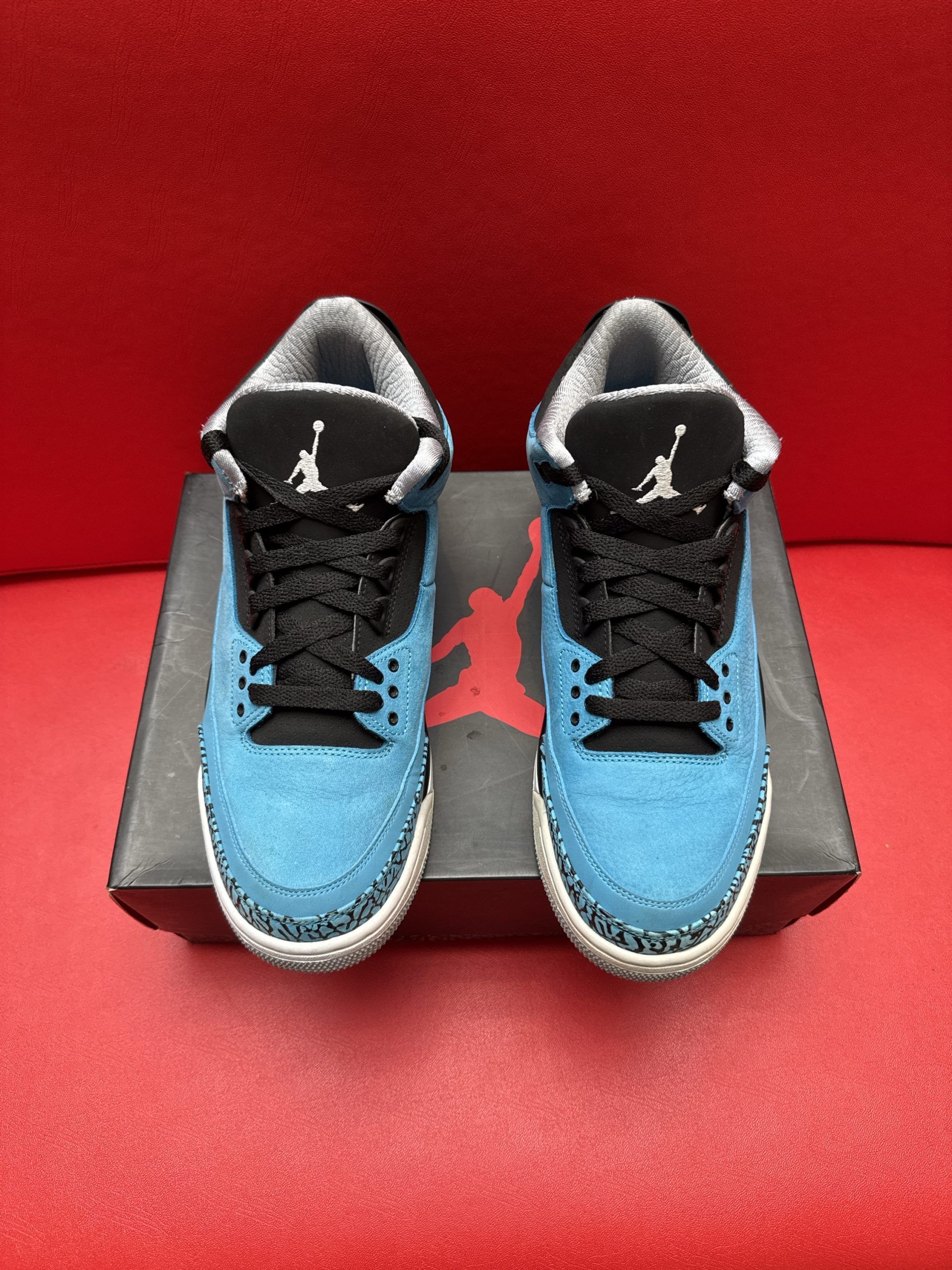 Baby blue and black Air Jordan 3 sneakers on a black box, gray sole. Red background.