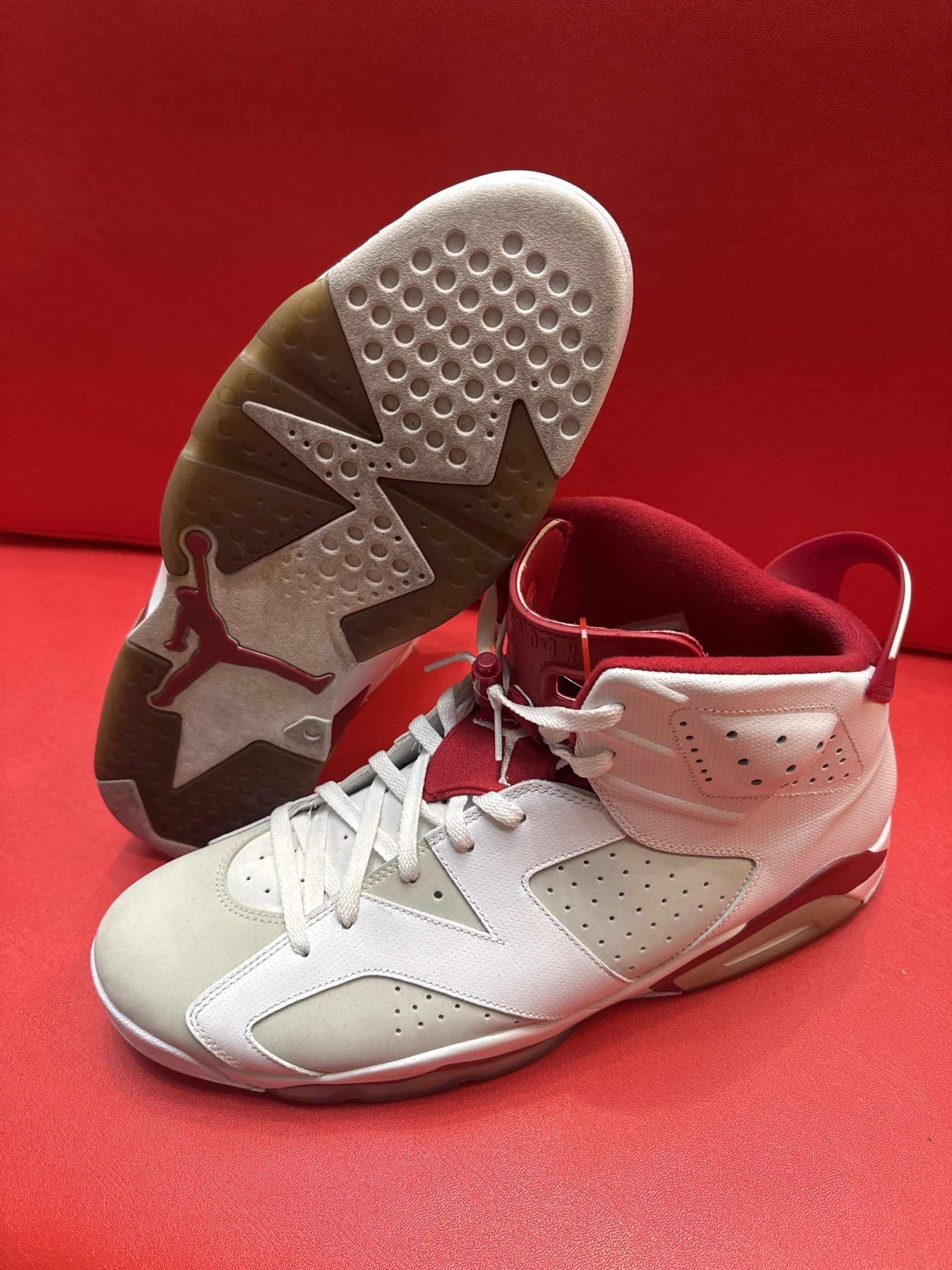White and red Air Jordan 6 sneakers on a red surface; sole visible.