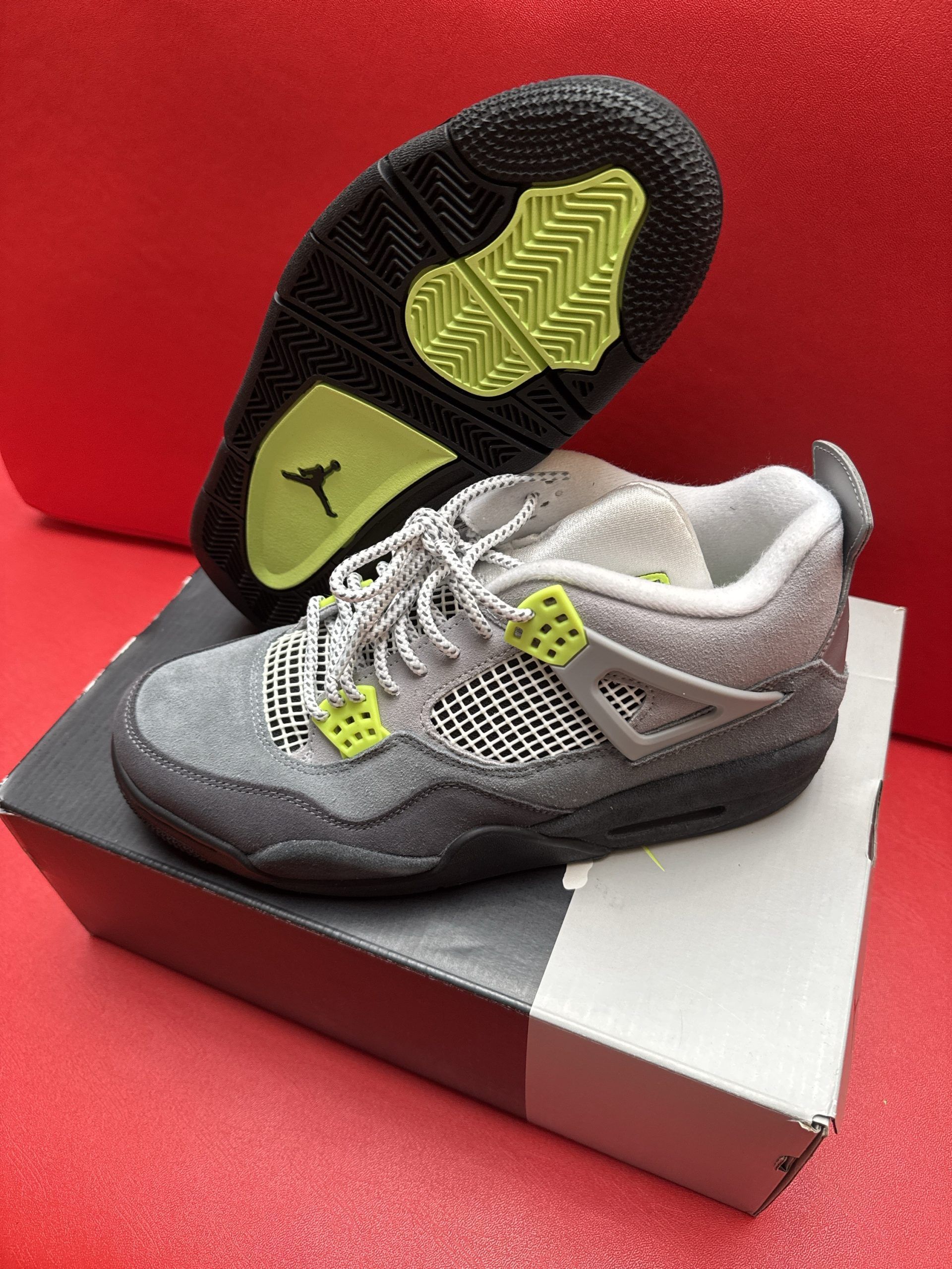 Gray and neon green Air Jordan 4 infant sneakers on a box, sole up.