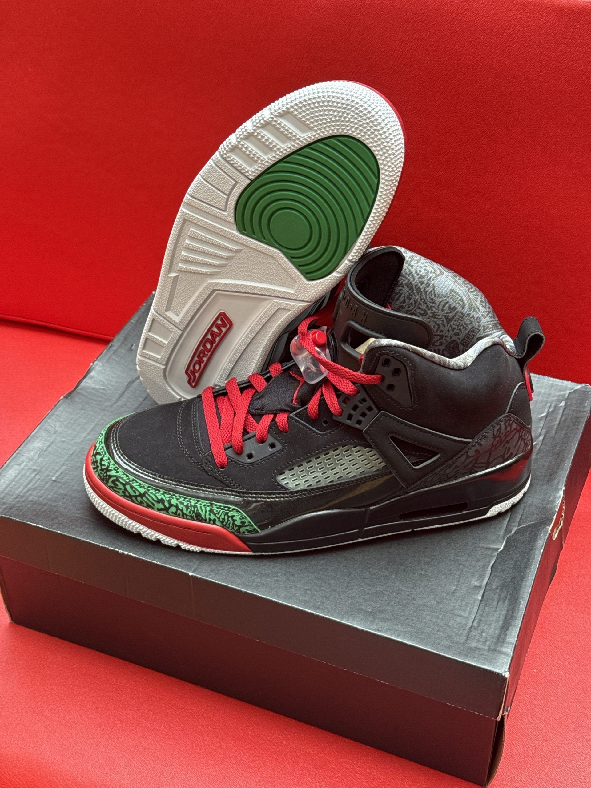 Black, red, and green Air Jordan sneakers on a box; one shoe displayed sole-up with green and white details.