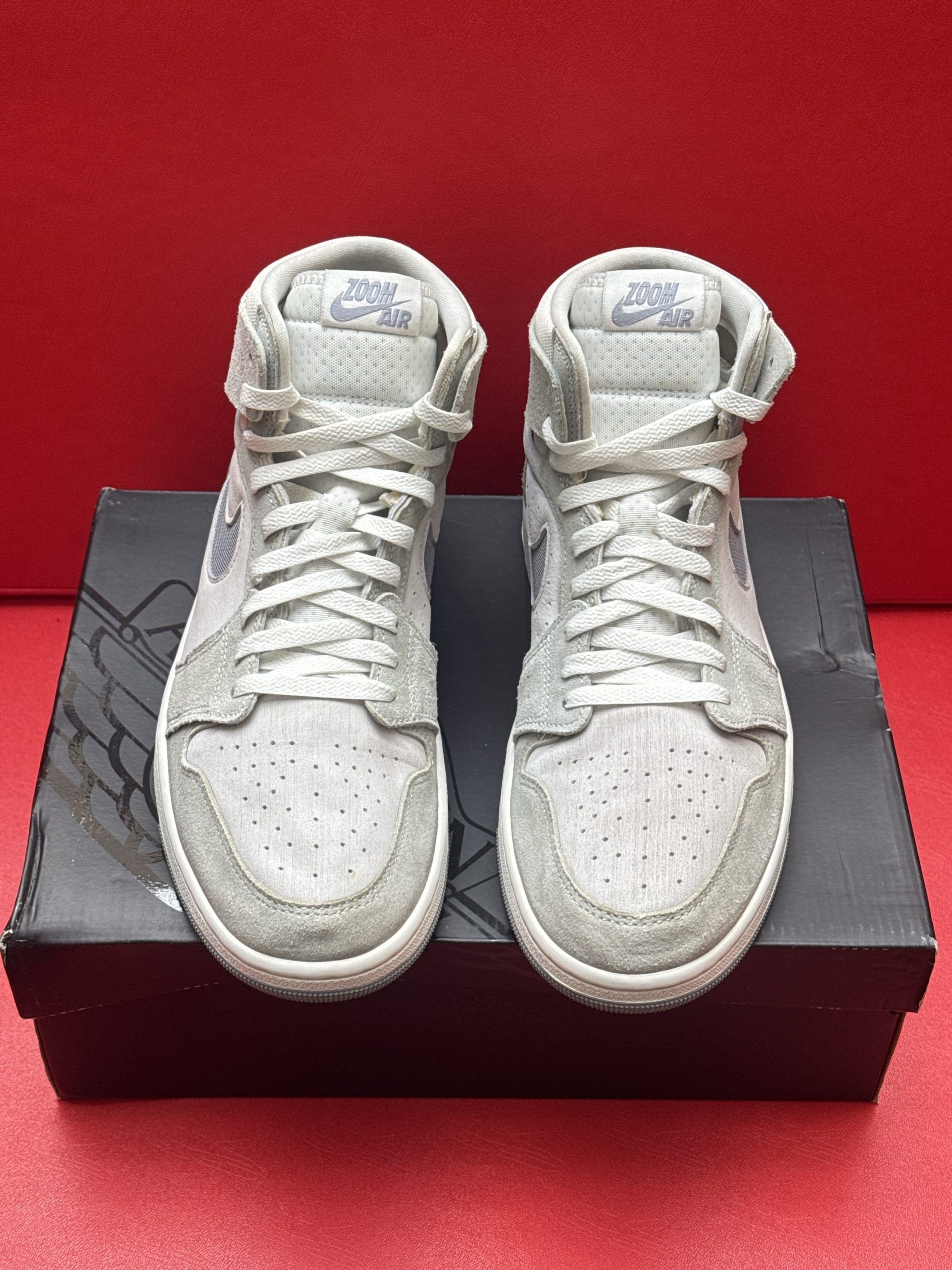 Pair of gray and white Air Jordan sneakers on top of a black shoebox, sole up.