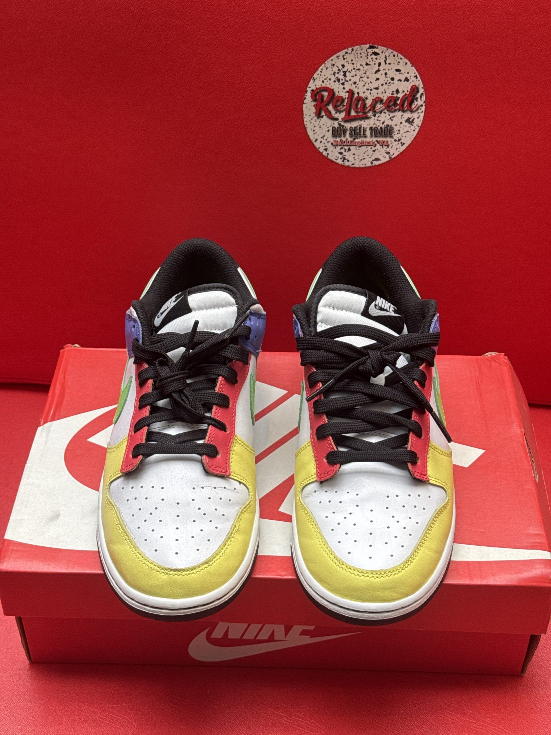 Nike Dunk Low sneakers with multi-colored panels, black sole, and shoebox on red surface.