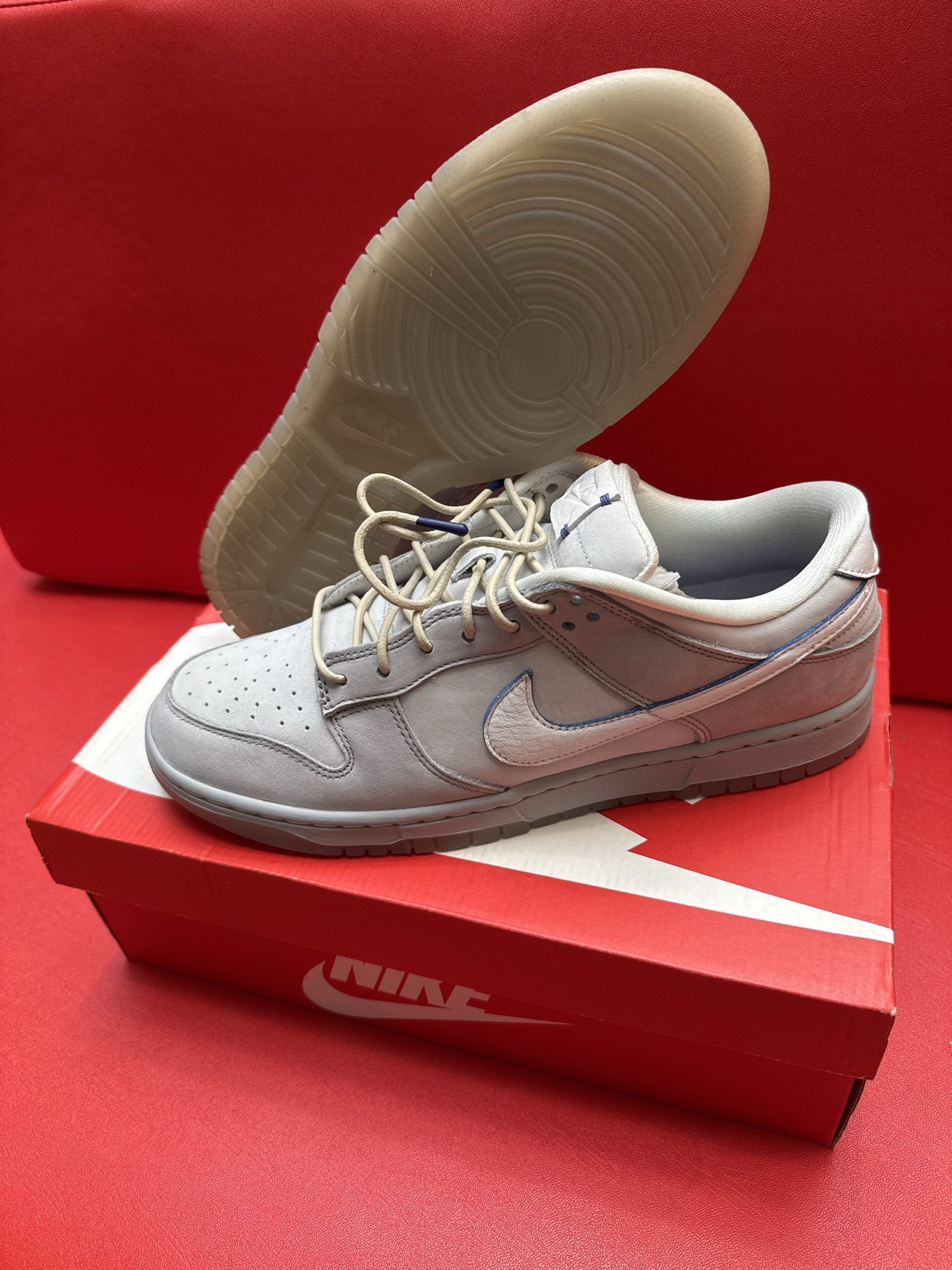 Grey Nike Dunk Low sneaker, sole, and red box on a red surface.