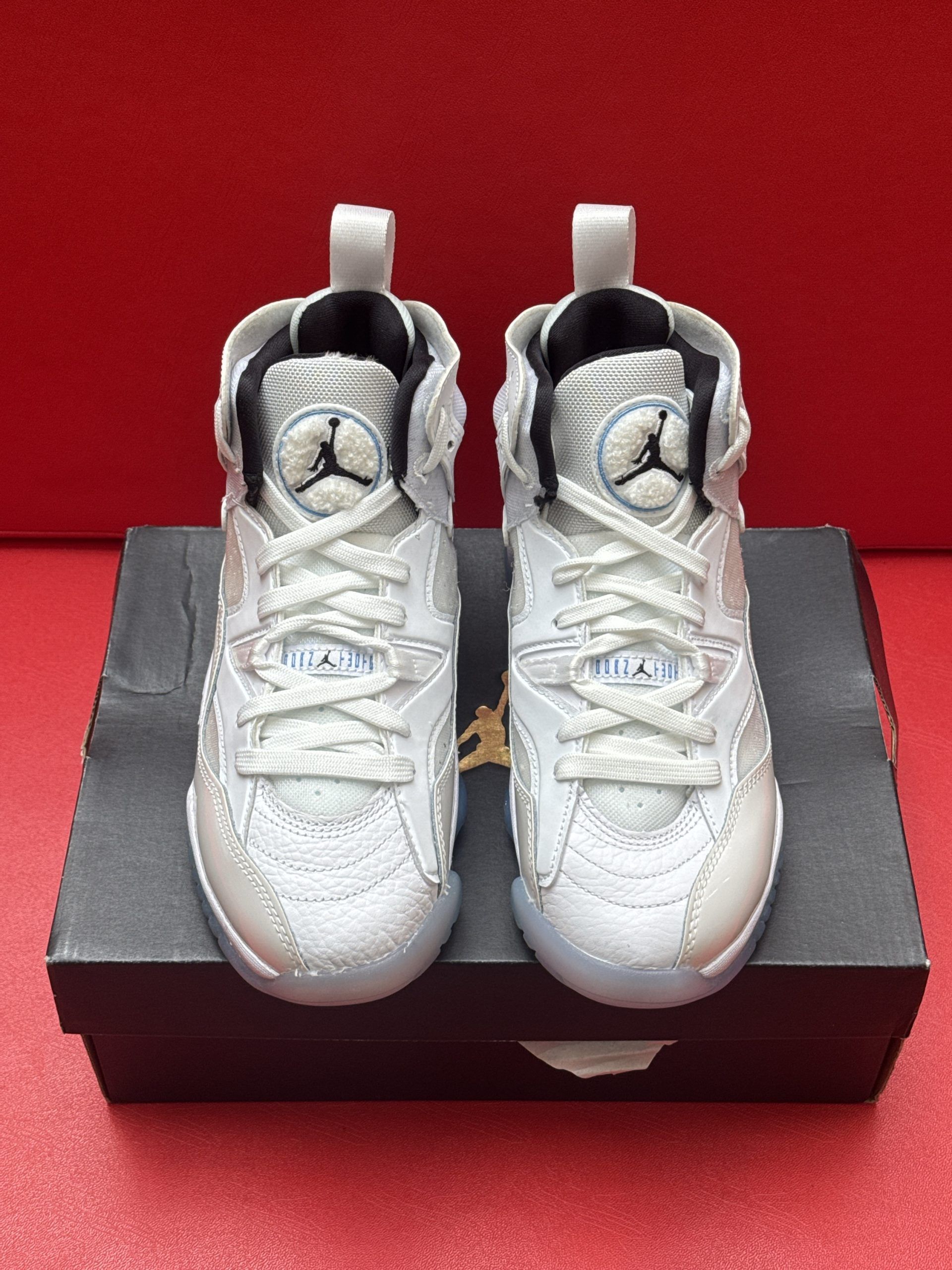 White and light blue Air Jordan shoes on a black box, set against a red background.