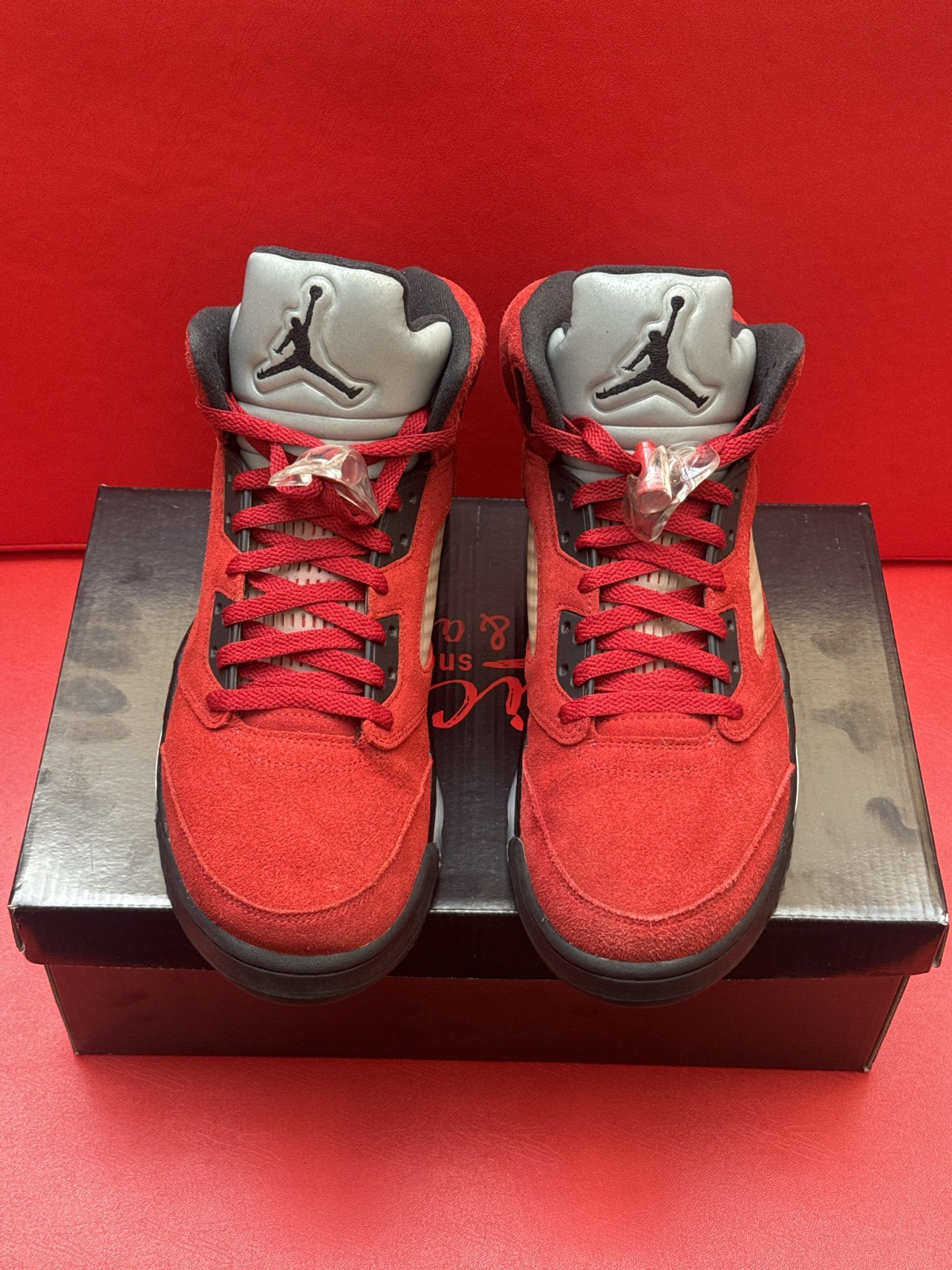 Red and black Air Jordan 5 sneakers, partially on a shoebox.