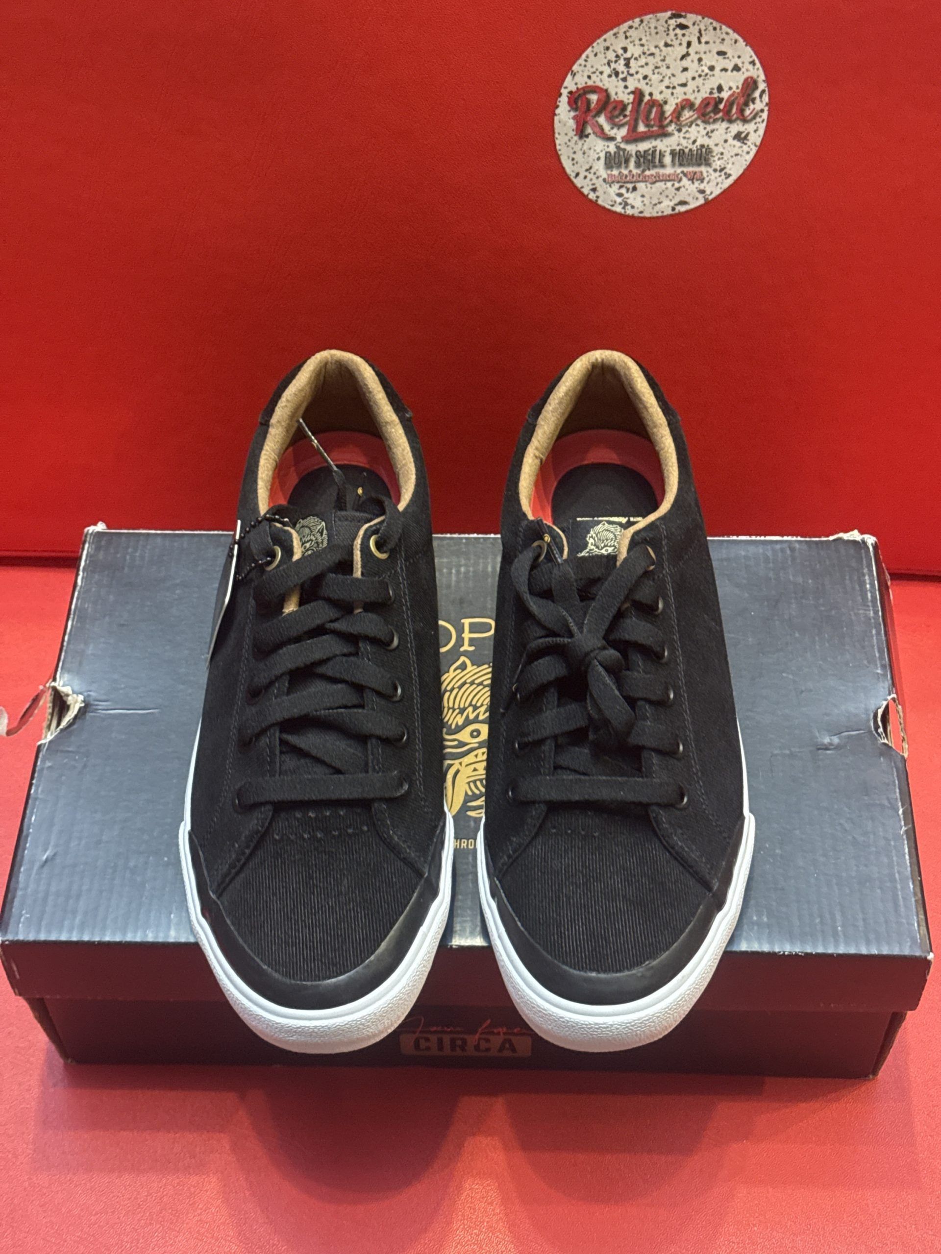 Black sneakers with white soles, laces, and a brown interior, atop a shoebox on a red surface.