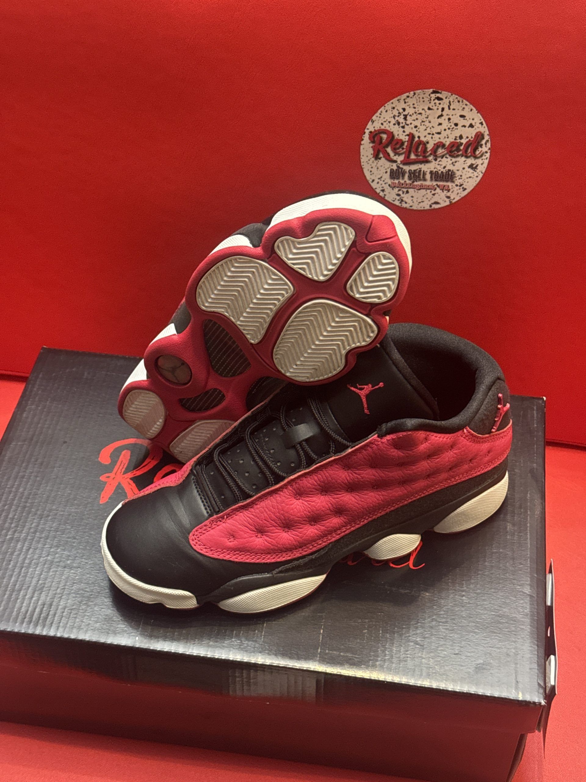 Red and black Air Jordan 13 sneakers on a shoebox, with the sole visible.