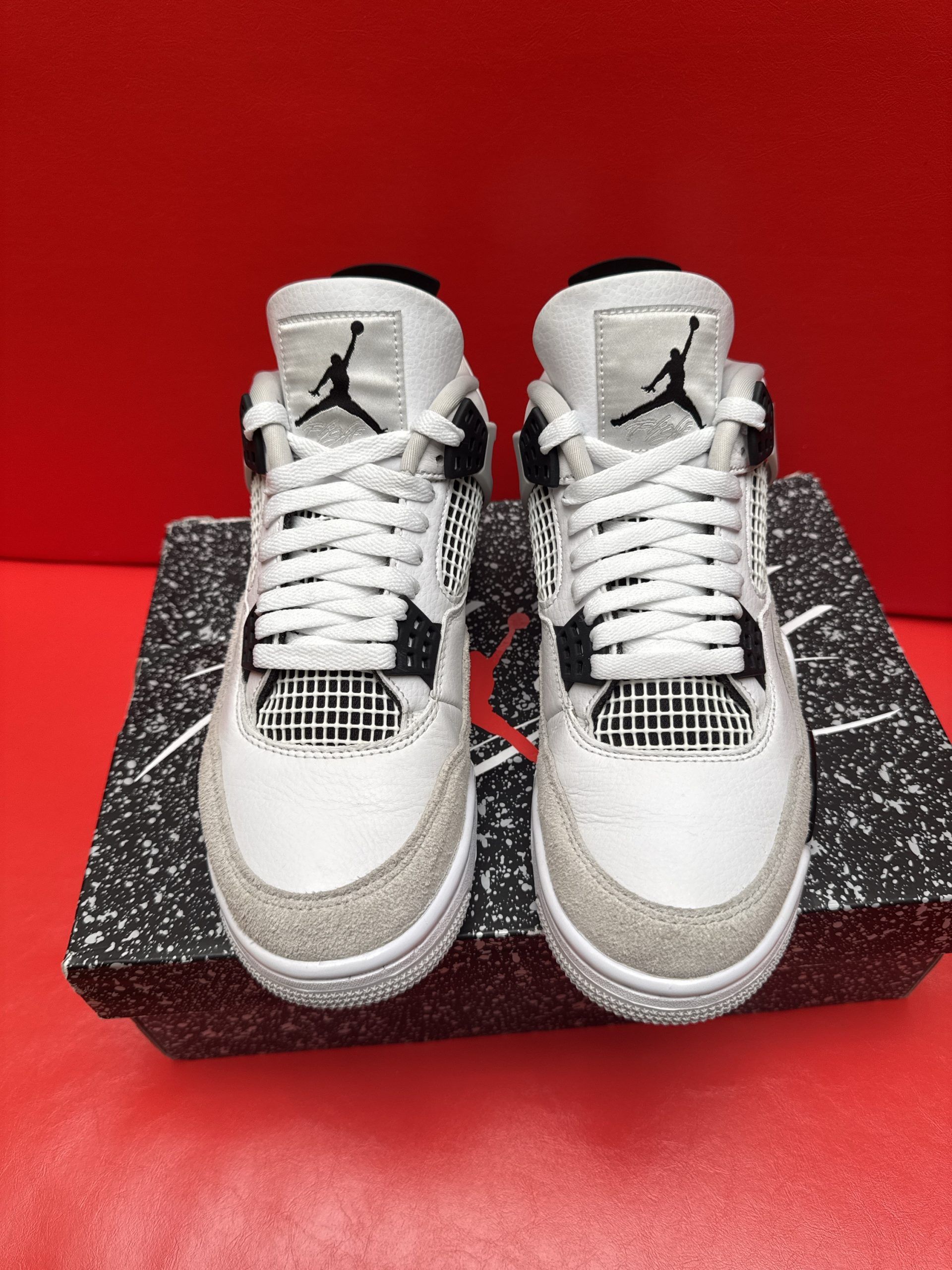 White and gray Air Jordan 4 sneakers on a speckled shoebox, with a red background.