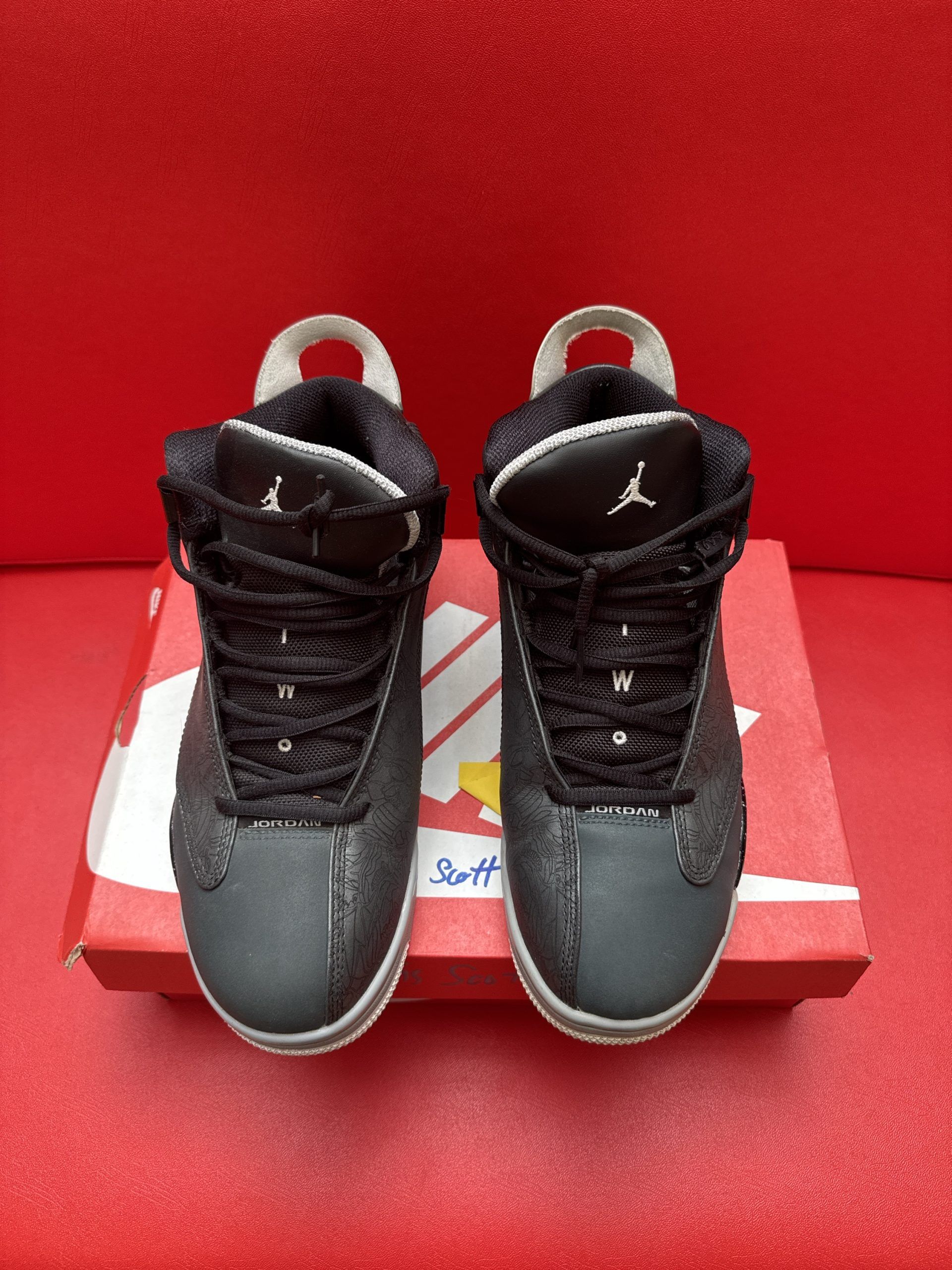 Black and grey Air Jordan sneakers, with the sole visible, on a red shoebox.
