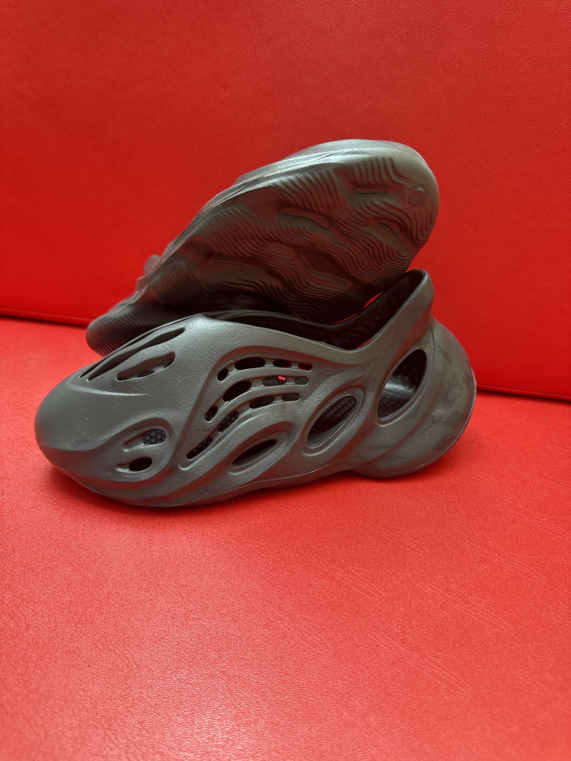 Black foam clog shoe on a red surface, with a heel portion flipped open.
