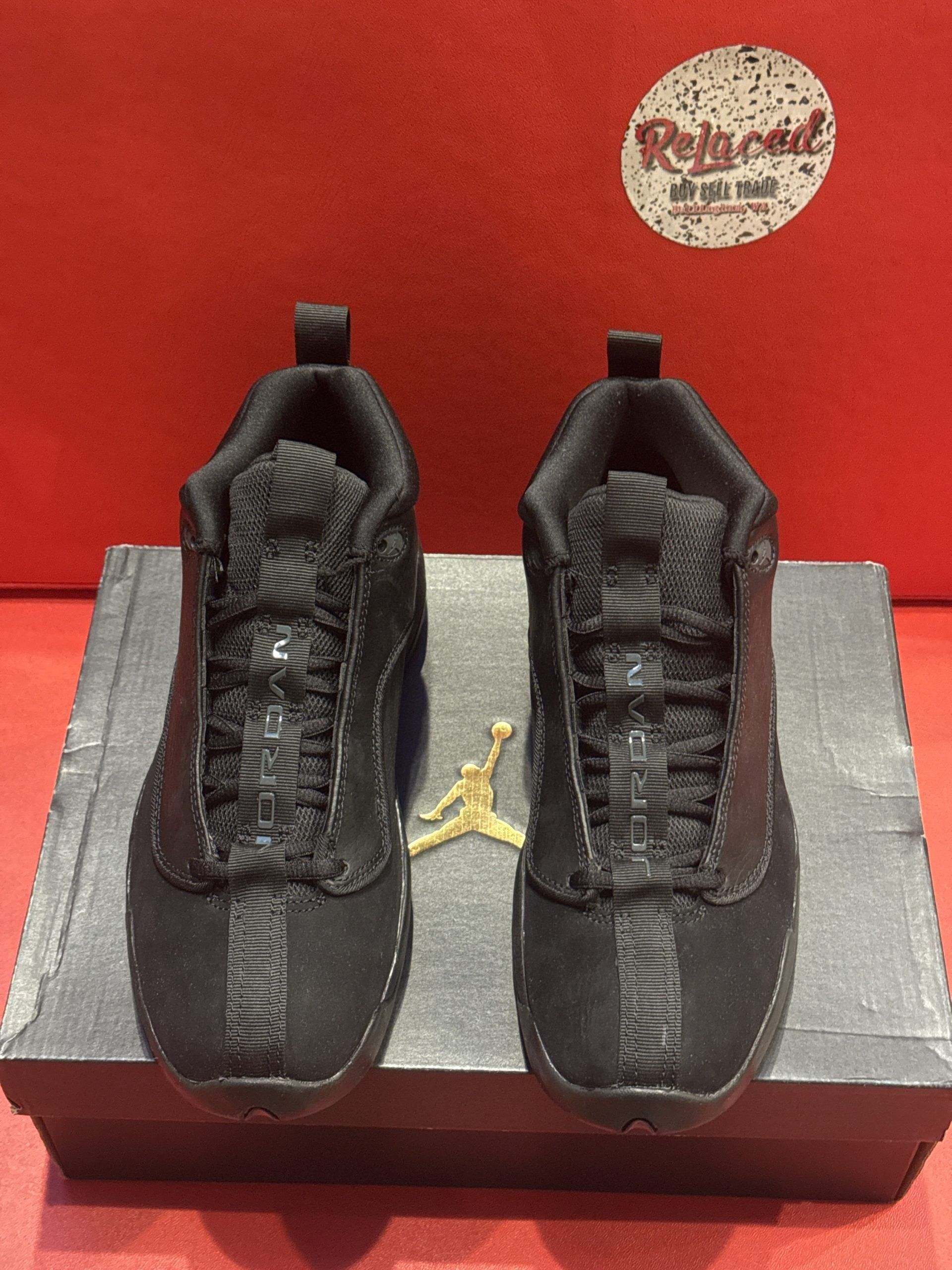 Black Jordan low-top sneakers on a shoebox. A red background is visible.