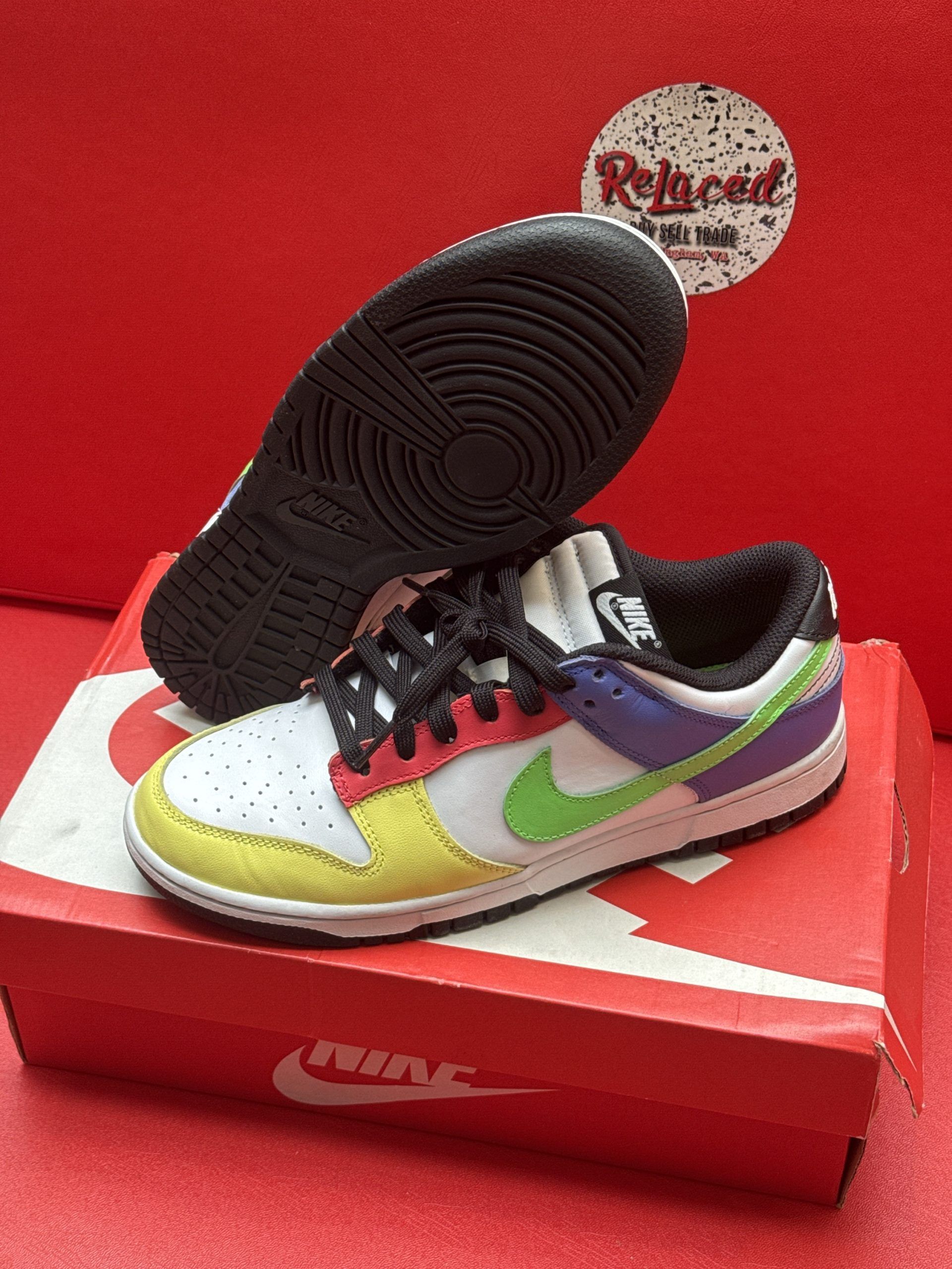 Nike Dunk Low sneakers with multi-colored panels, black sole, and shoebox on red surface.